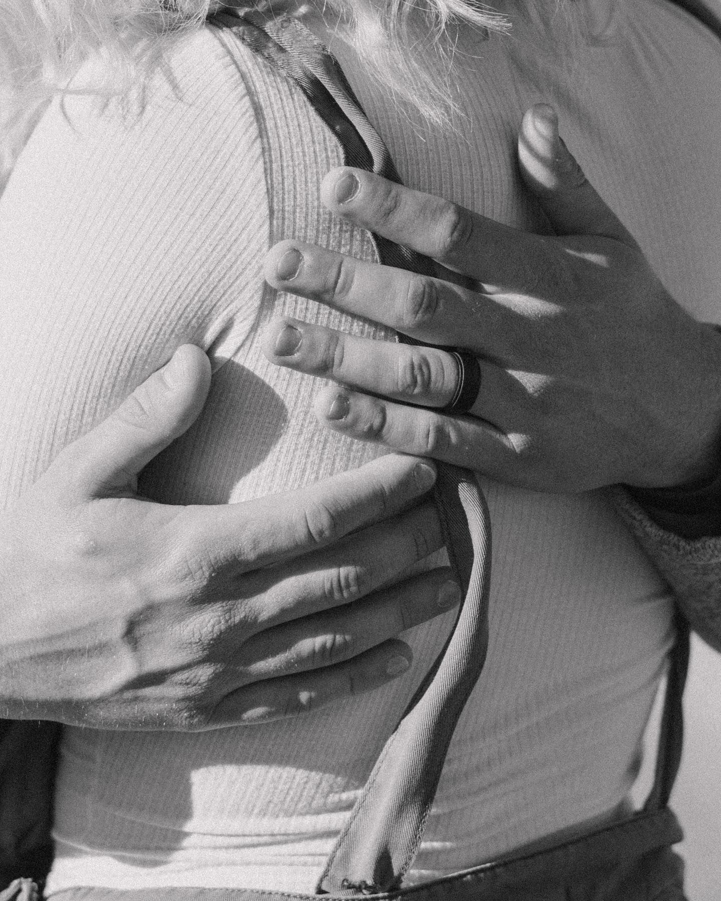 Black and white close-up of hands tenderly placed on a torso wearing a white ribbed top.