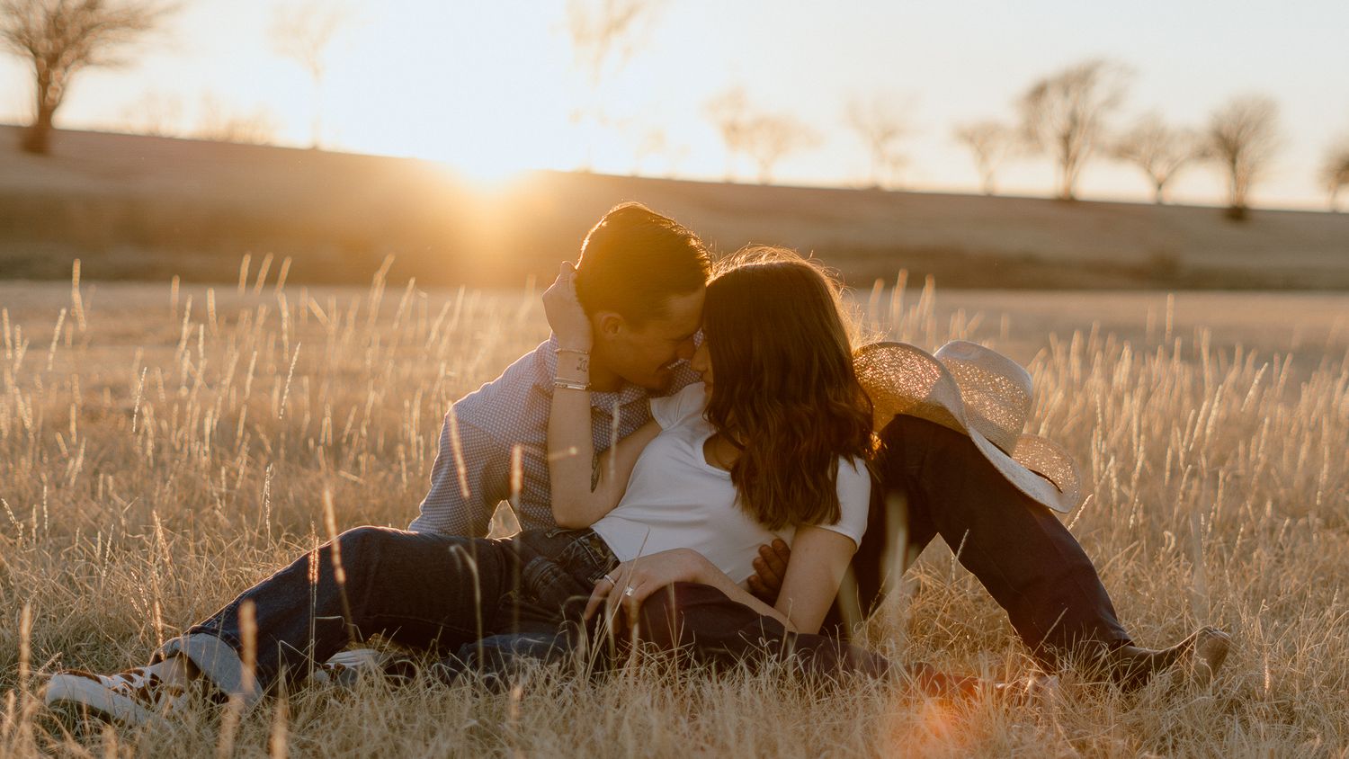 Couple lying in golden wheat field during sunset photography session.