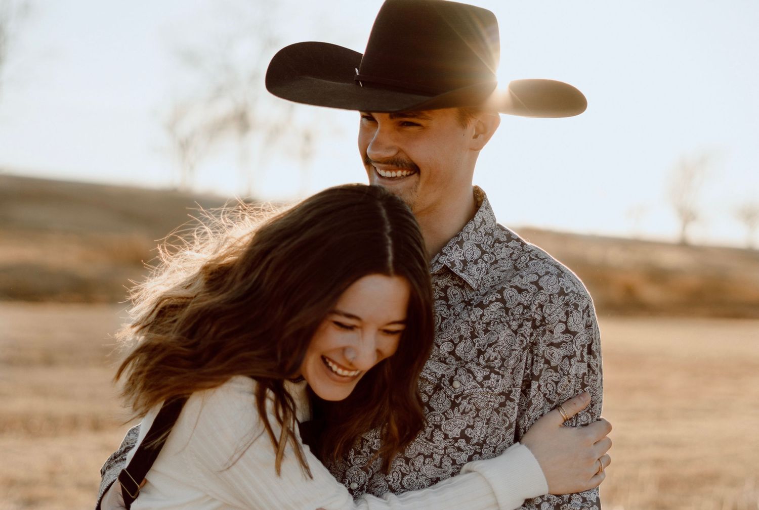 Romantic couple embracing in a rustic field at golden hour.