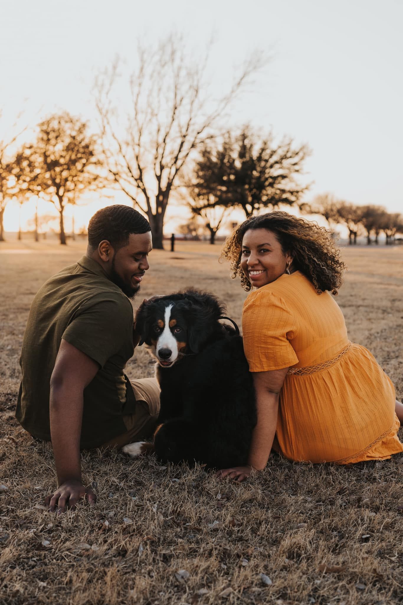 Couple and their dog relax together in autumn field at sunset.