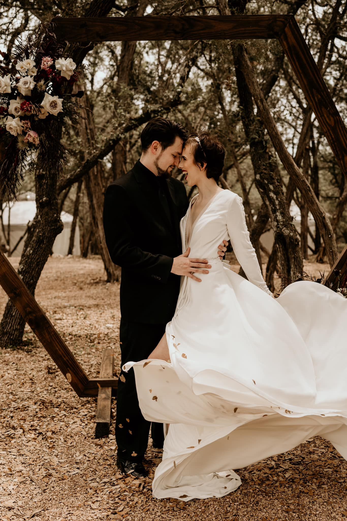 White wedding dress flows dramatically during outdoor couple's photoshoot among trees.