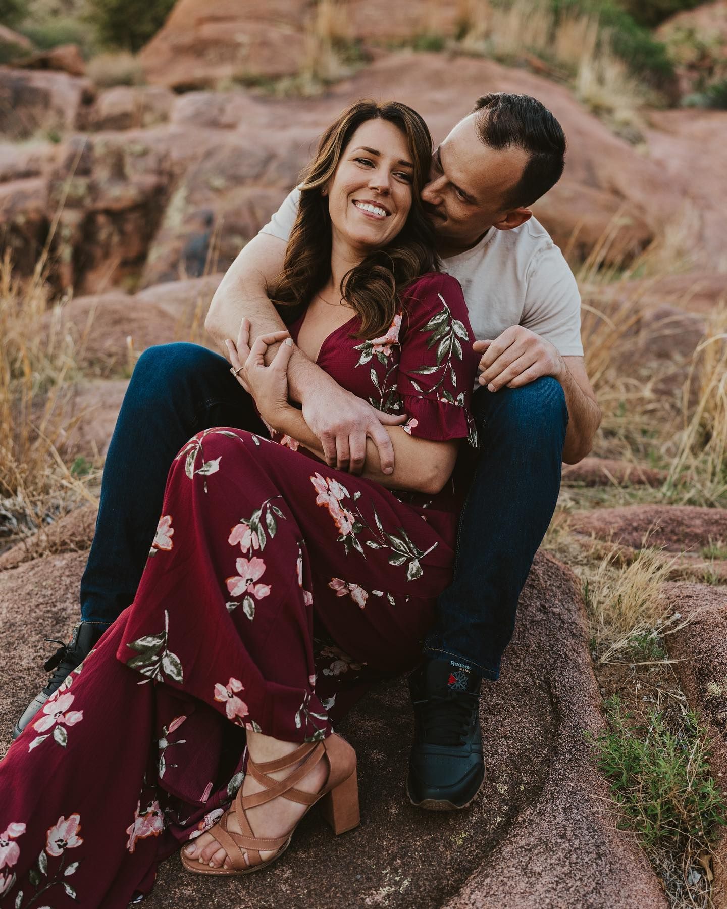 Couple in casual attire sharing intimate moments on red rock formations.