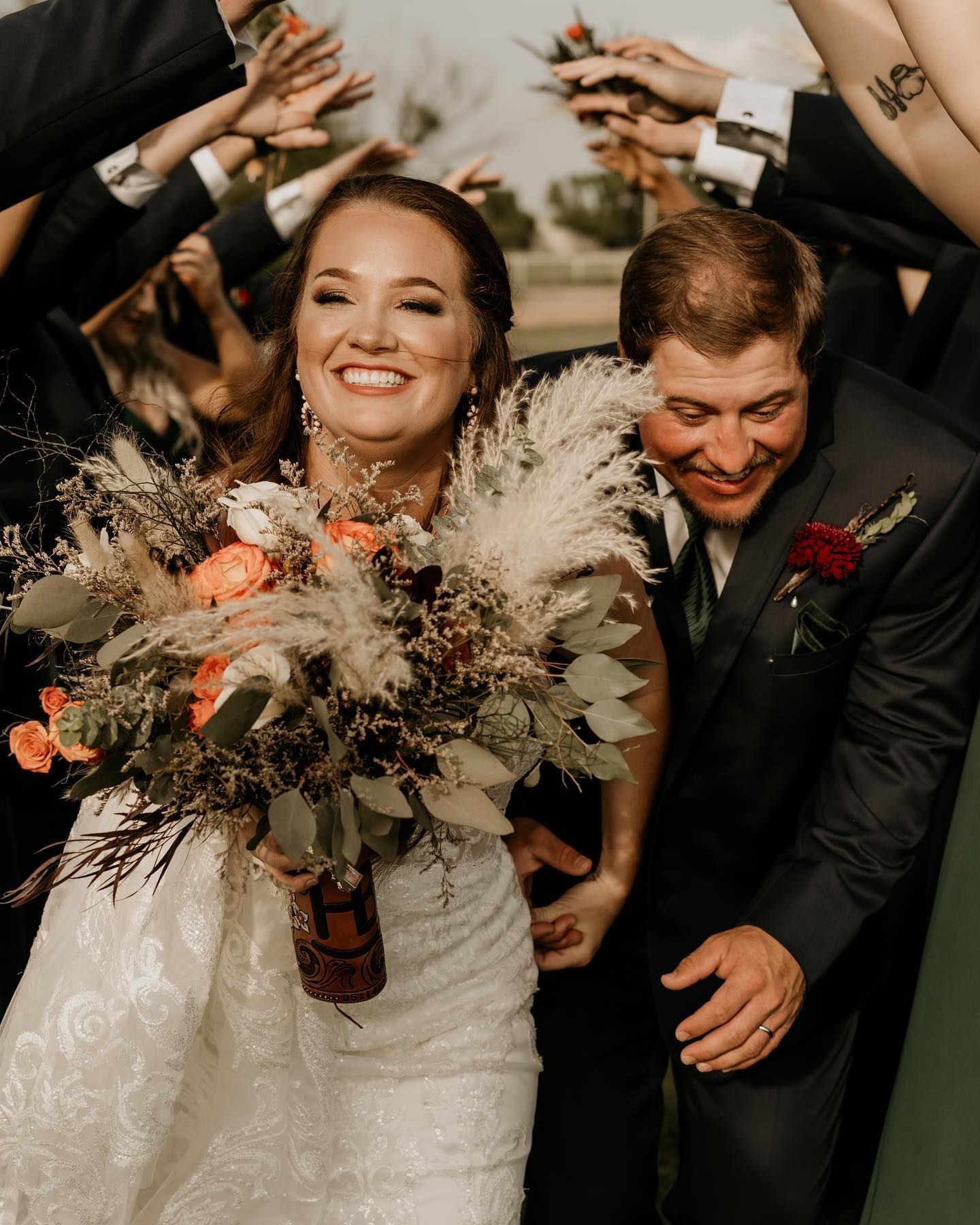 Wedding party laughs and celebrates with dried flower bouquets in a candid moment.