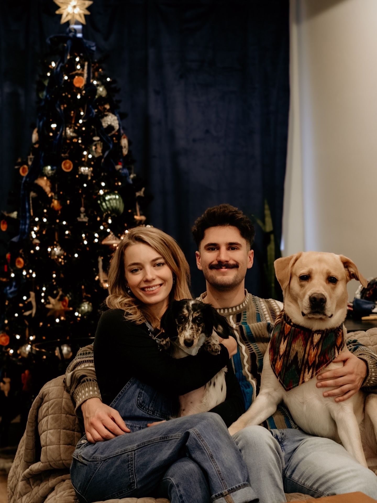 Family and dogs pose for holiday photos in front of decorated Christmas tree.