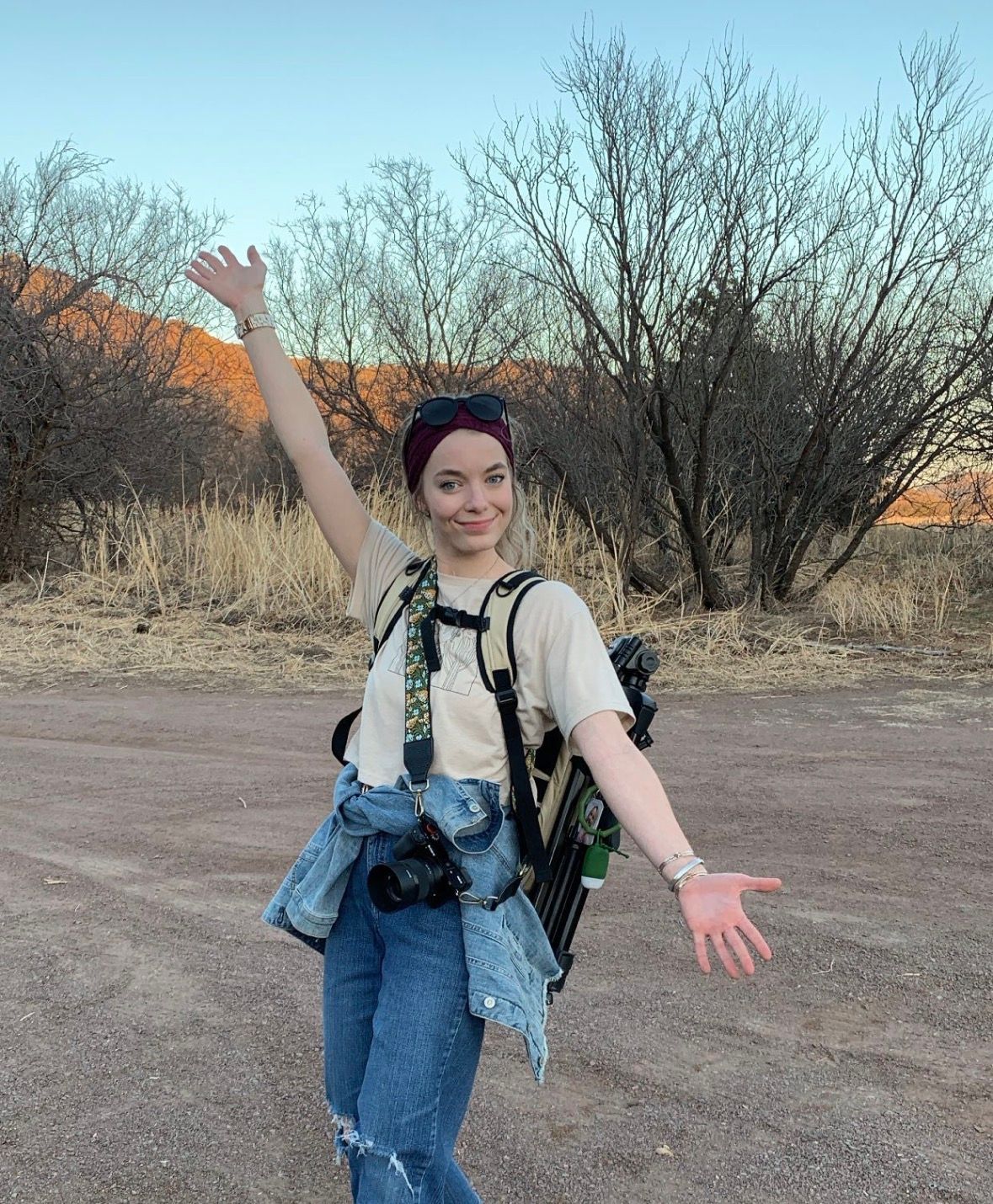 Person in overalls walks through desert landscape with backpack.