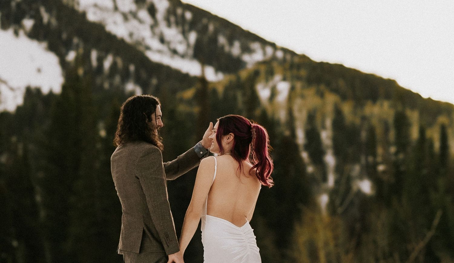 Couple embraces in a snowy mountain landscape during sunset.