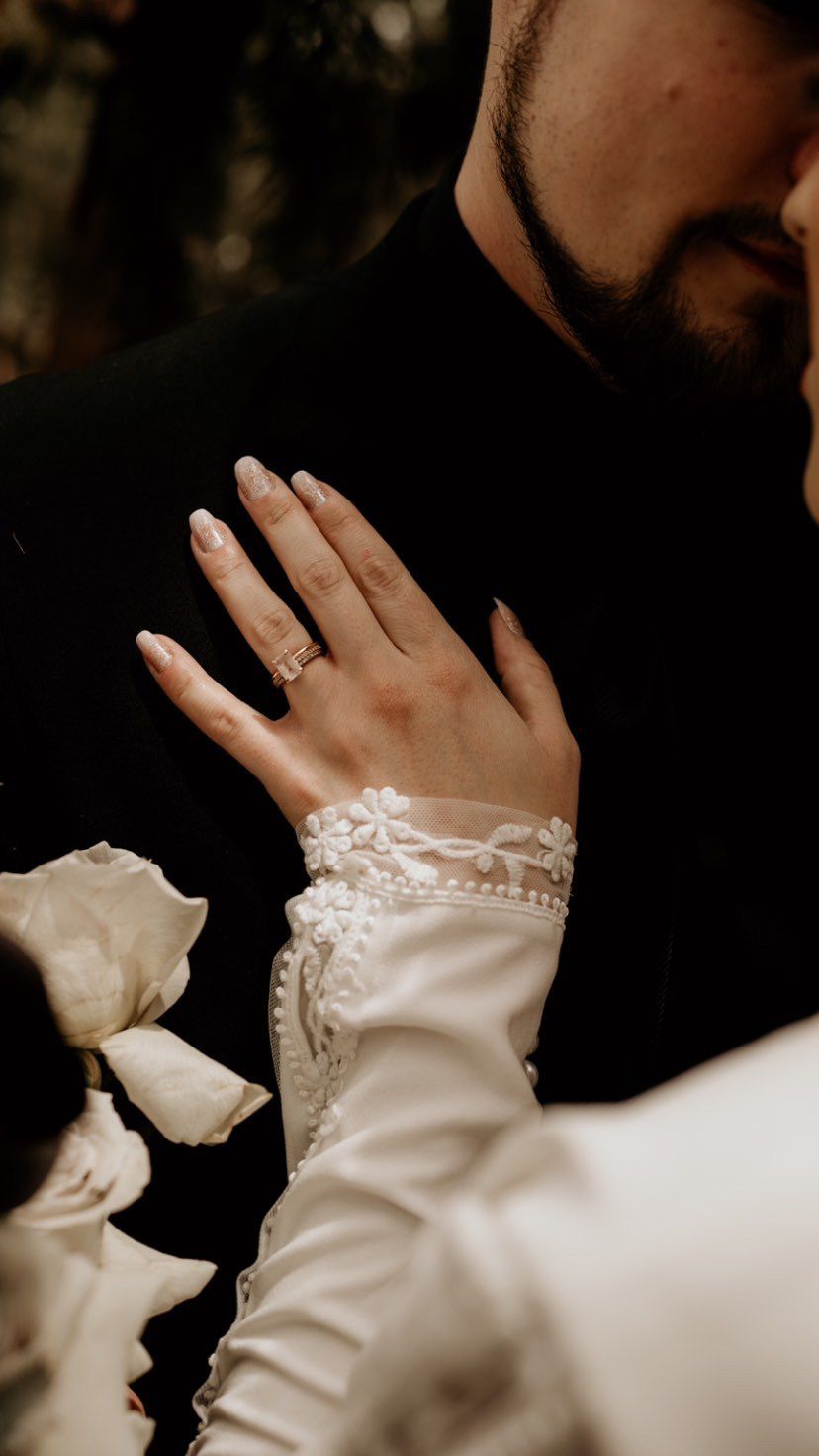 Close-up detail of delicate lace sleeves and an engagement ring in soft lighting.