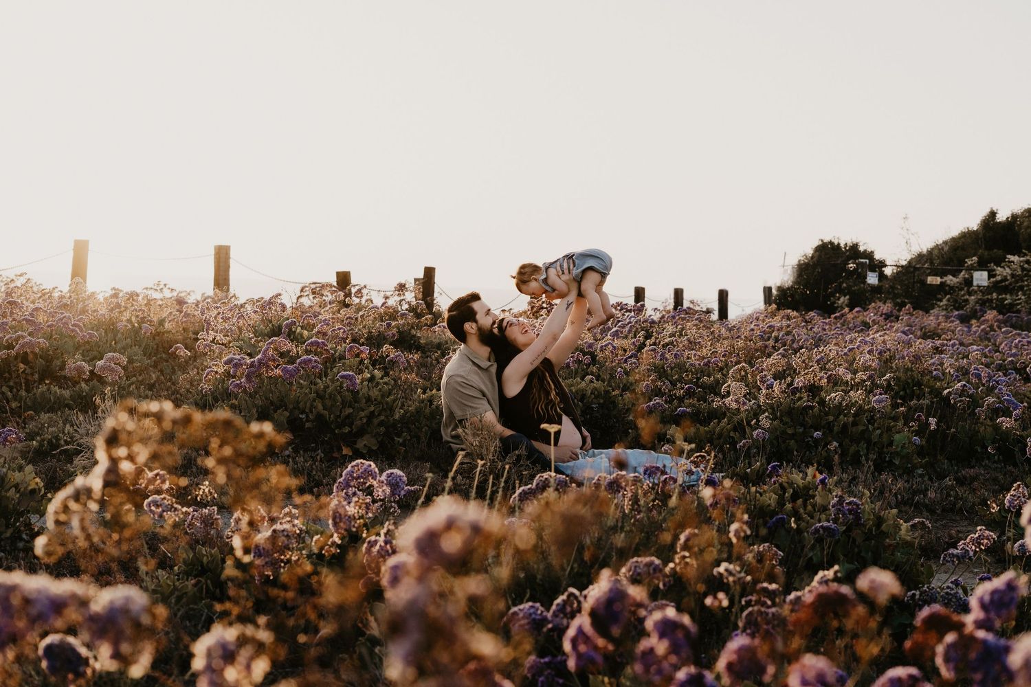 A man lifts a child joyfully in a blooming wildflower field during golden hour.