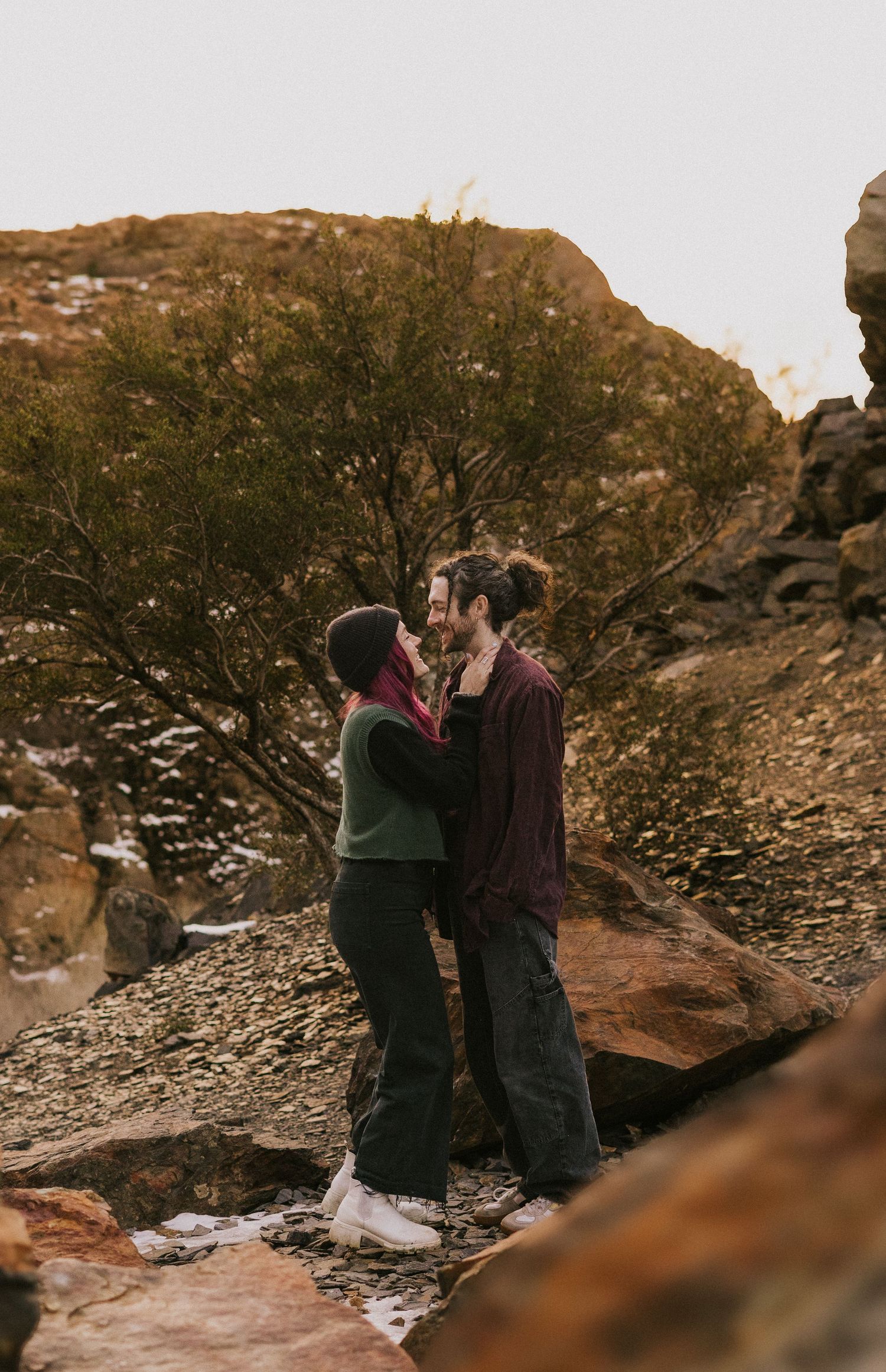 Couple embracing on rocky terrain during a desert sunset photoshoot.