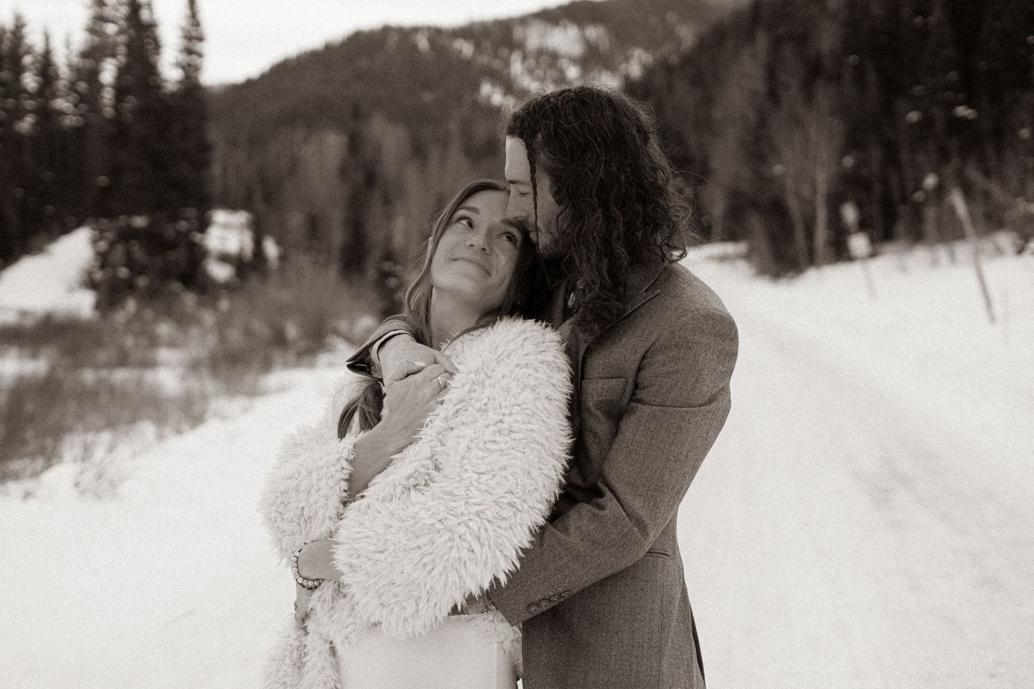 Intimate winter photoshoot with couple in snow-covered mountain setting.