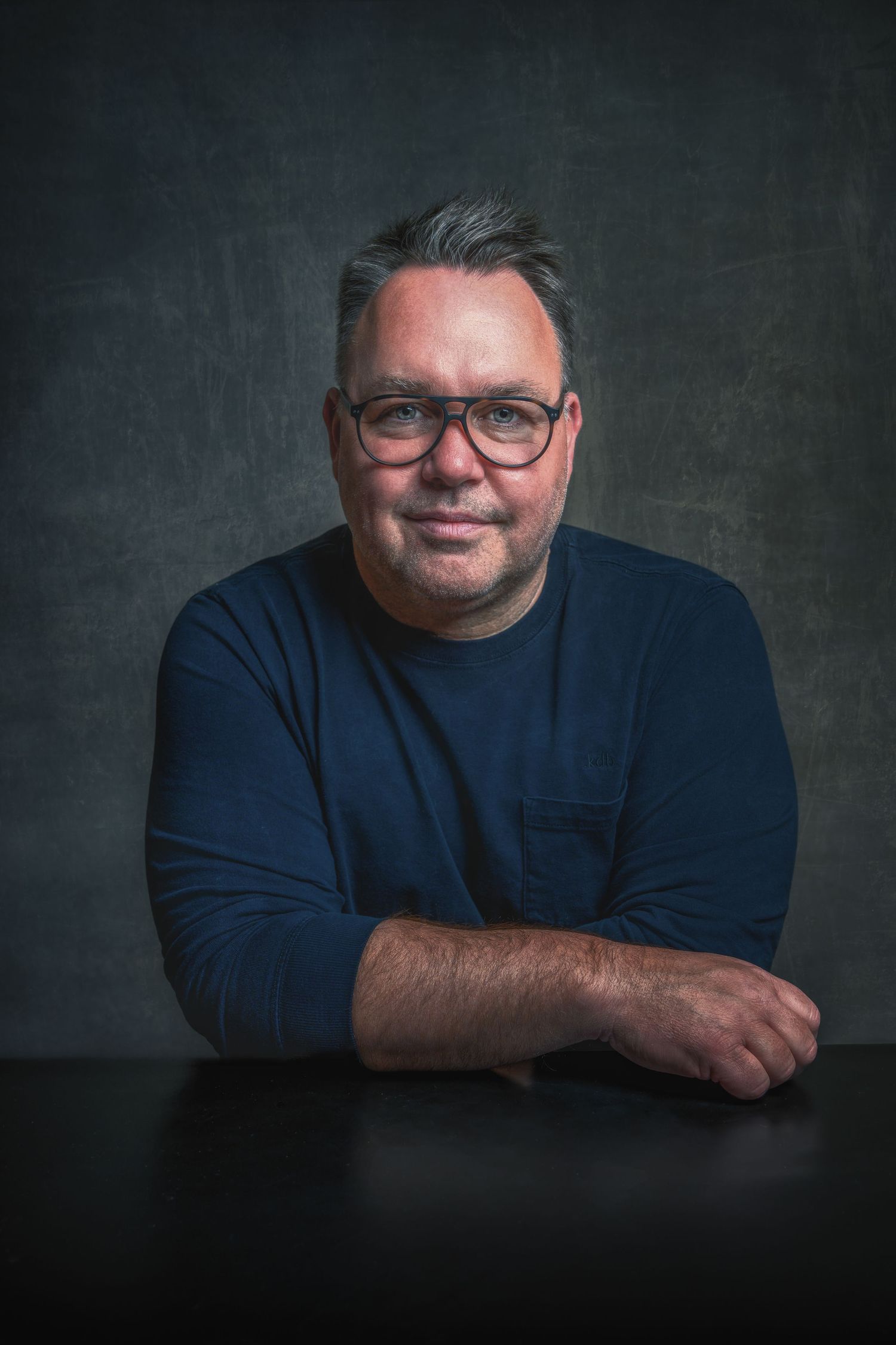 Studio headshots of a person wearing glasses and navy shirt against dark backdrop.
