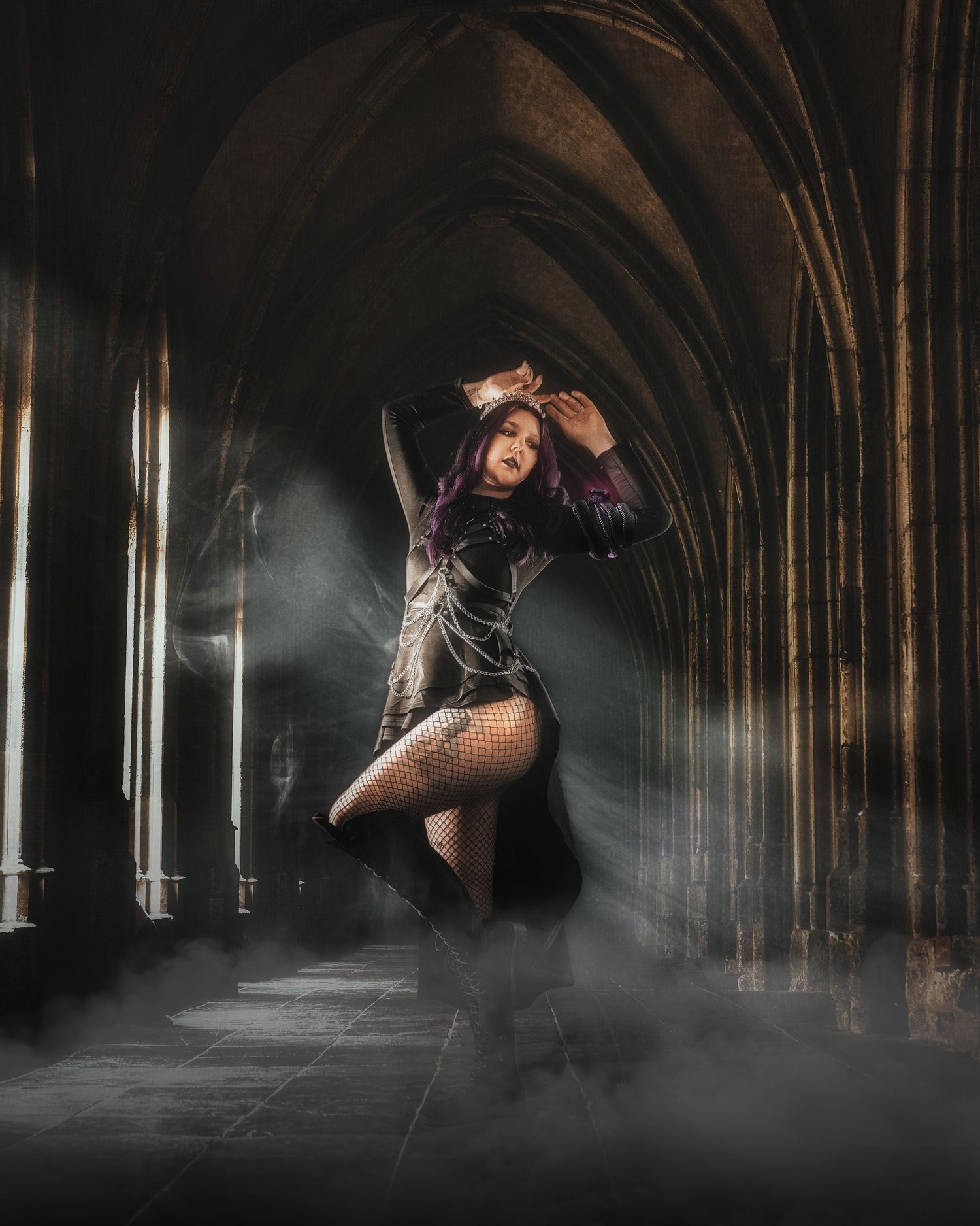 A woman with purple hair poses dramatically in gothic arched hallway wearing fishnet stockings and black corset amid misty atmosphere.