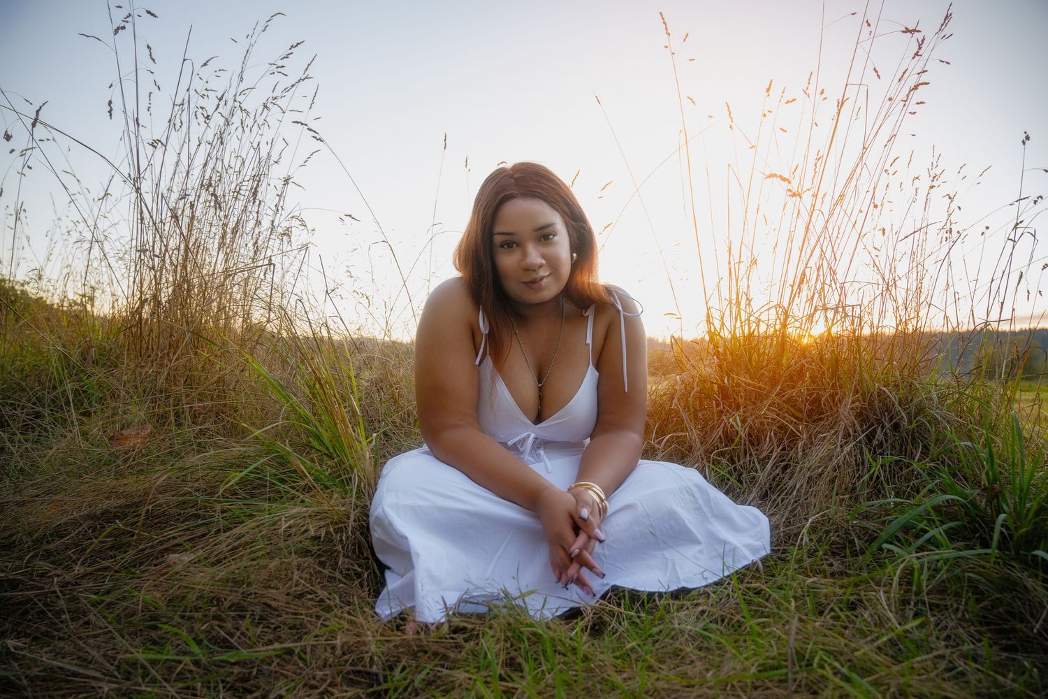 Woman in white dress poses gracefully among tall grass during golden hour photoshoot.