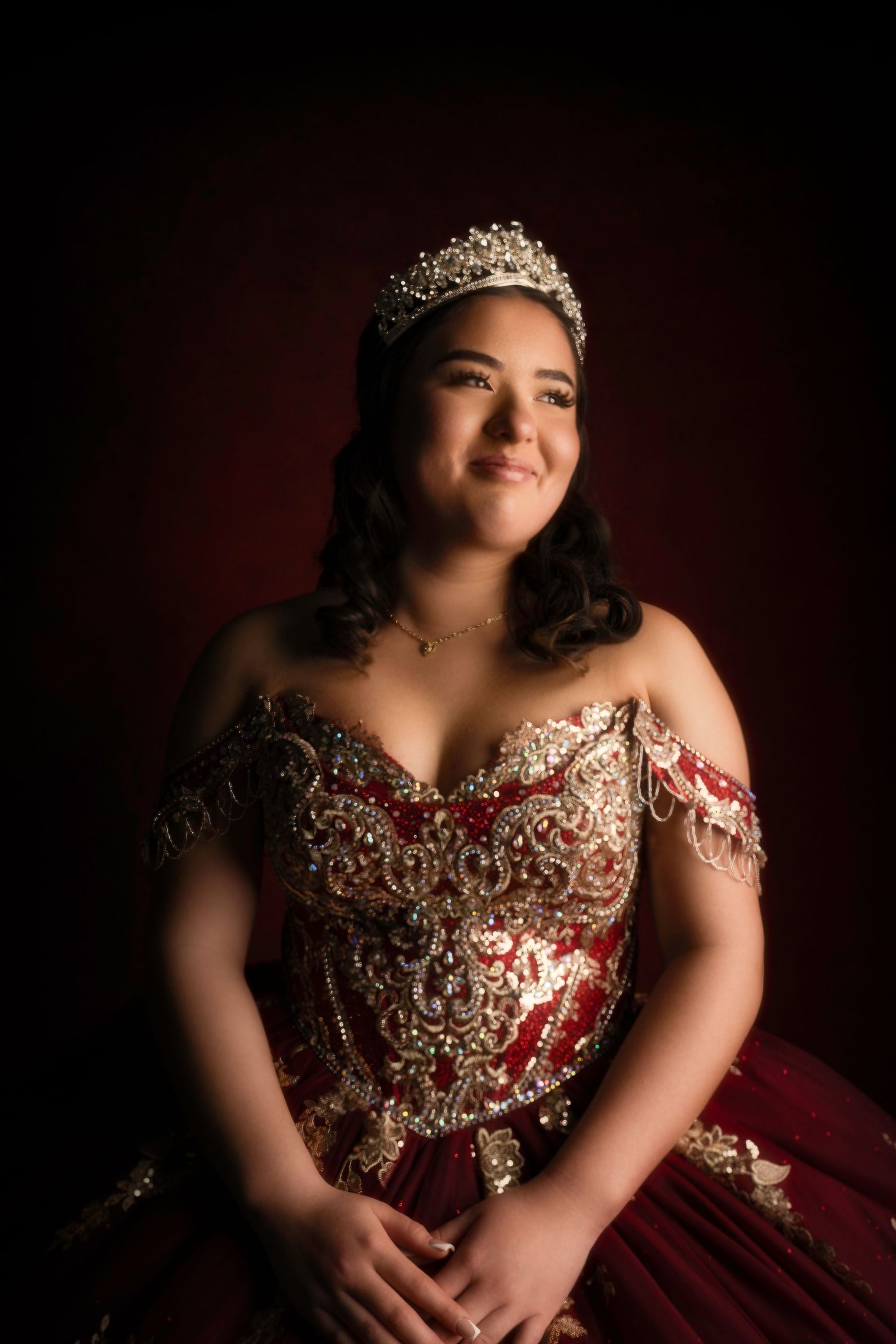 Elegant quinceañera portrait session featuring a sparkly red and gold ball gown and tiara.