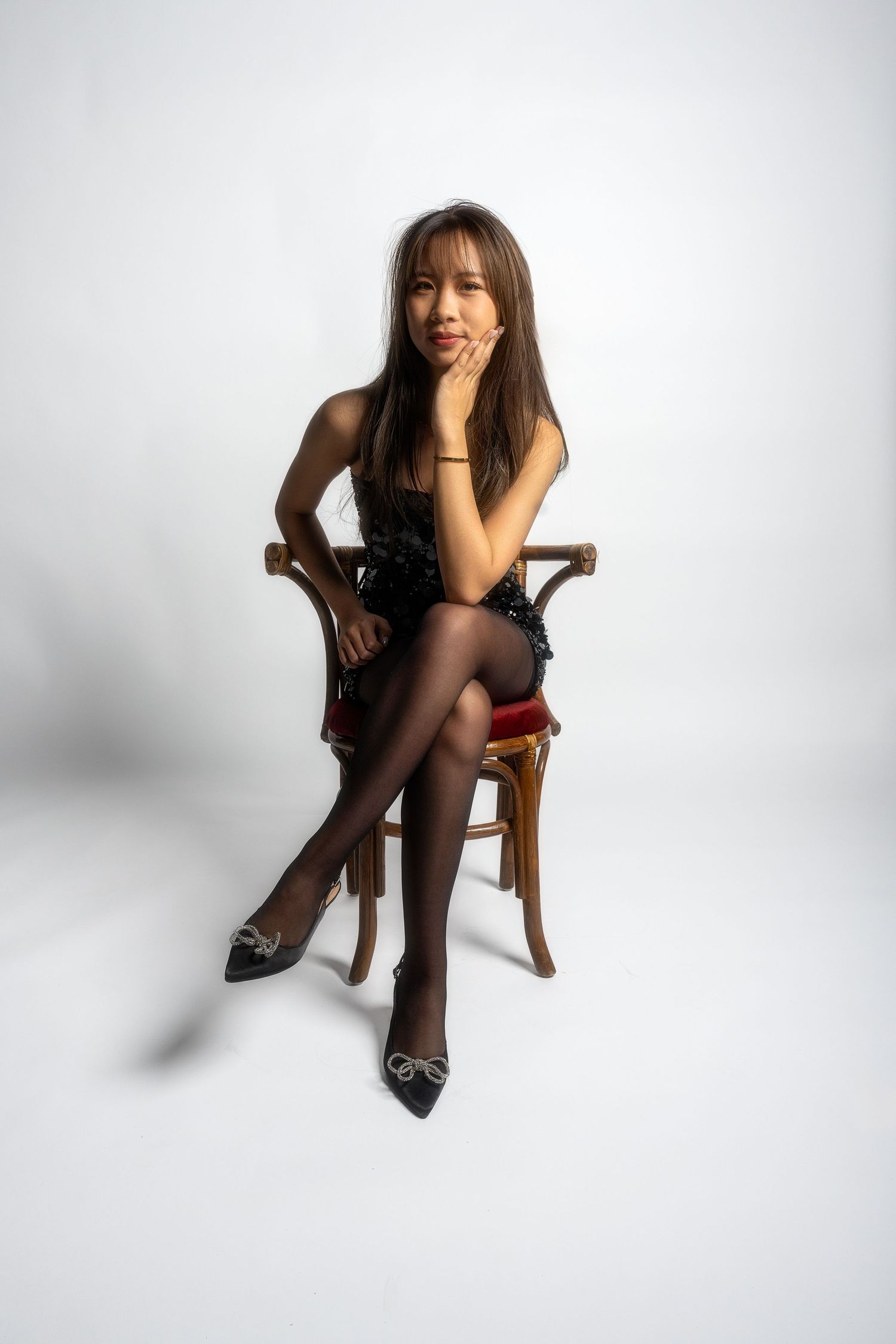 Fashion photo series of model in black outfit posing on wooden chair against white background.