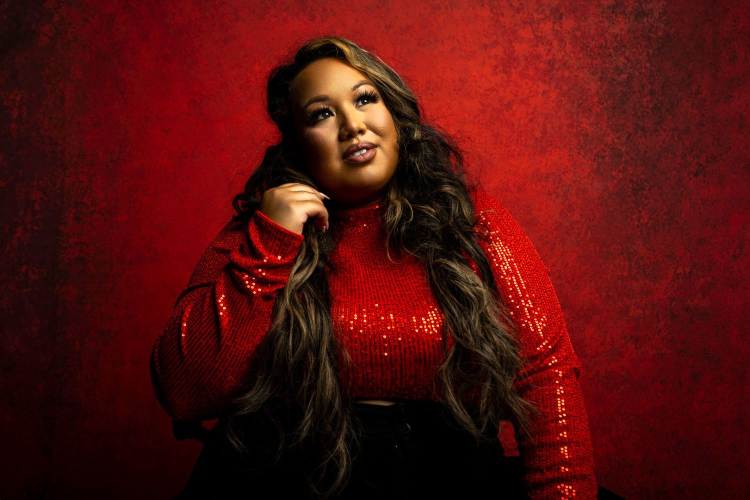 Glamour portrait against red background with sparkly dress and dramatic lighting.