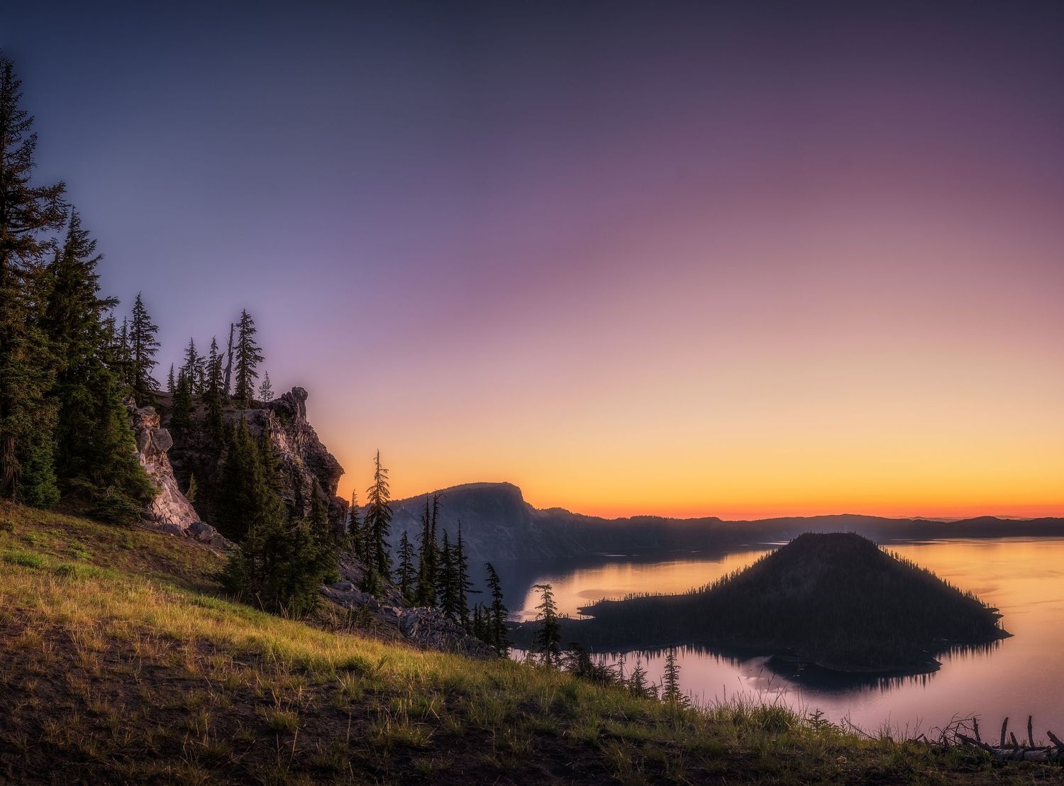 Panoramic twilight landscape of a tranquil lake surrounded by mountains under a purple sky.