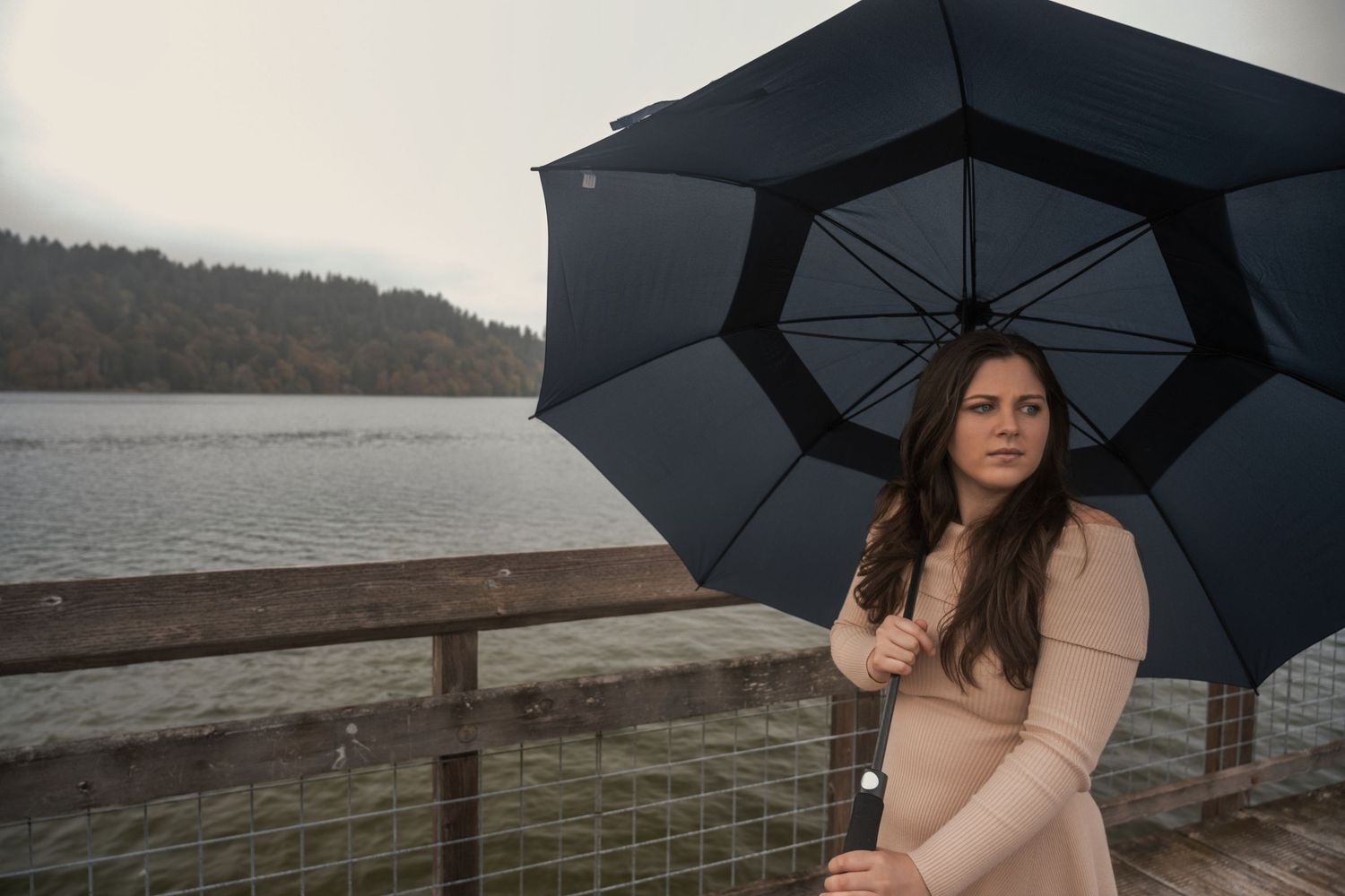 Moody photoshoot with black umbrella by waterfront on overcast day.