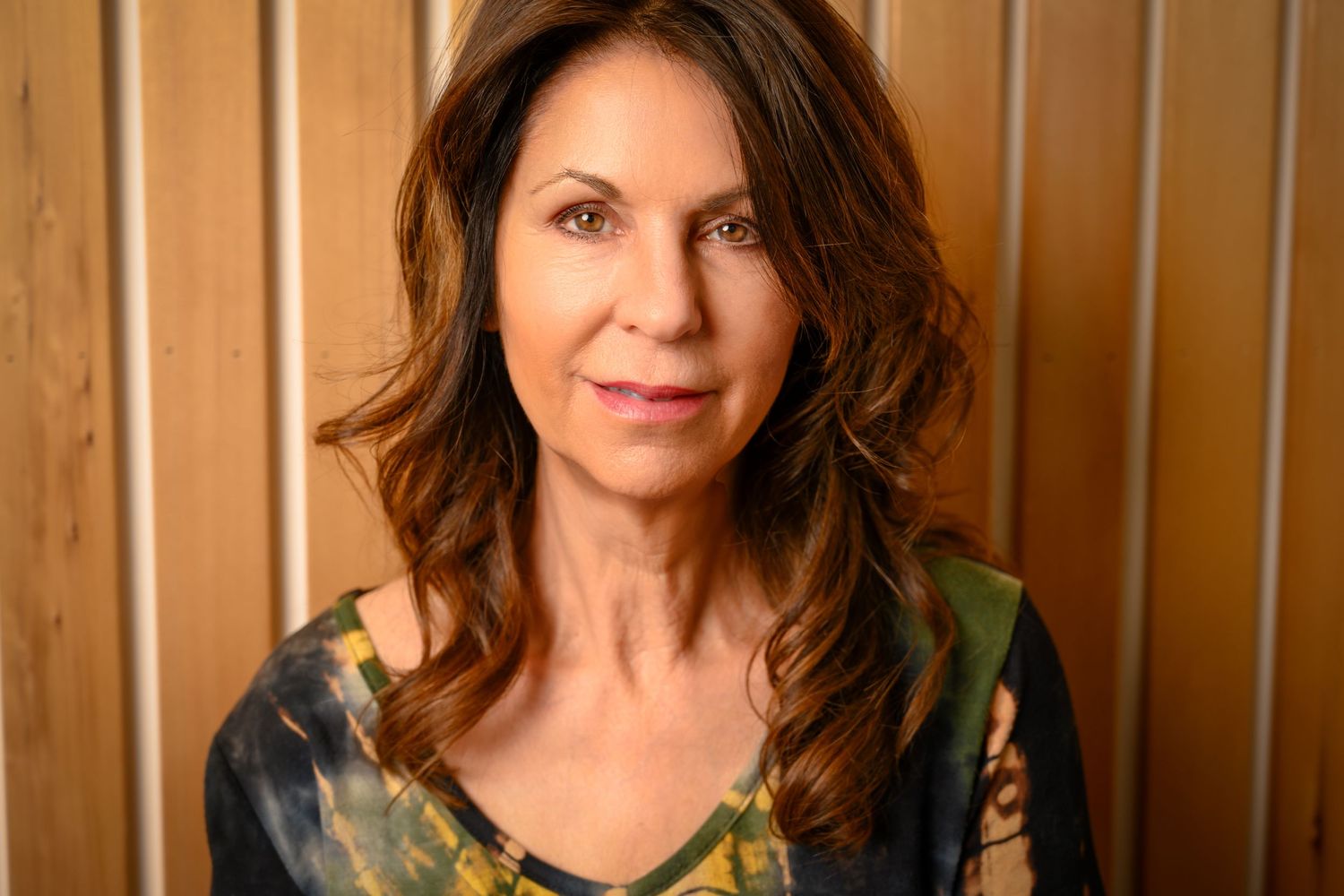 Woman in black top smiling warmly against a wooden paneled wall background.
