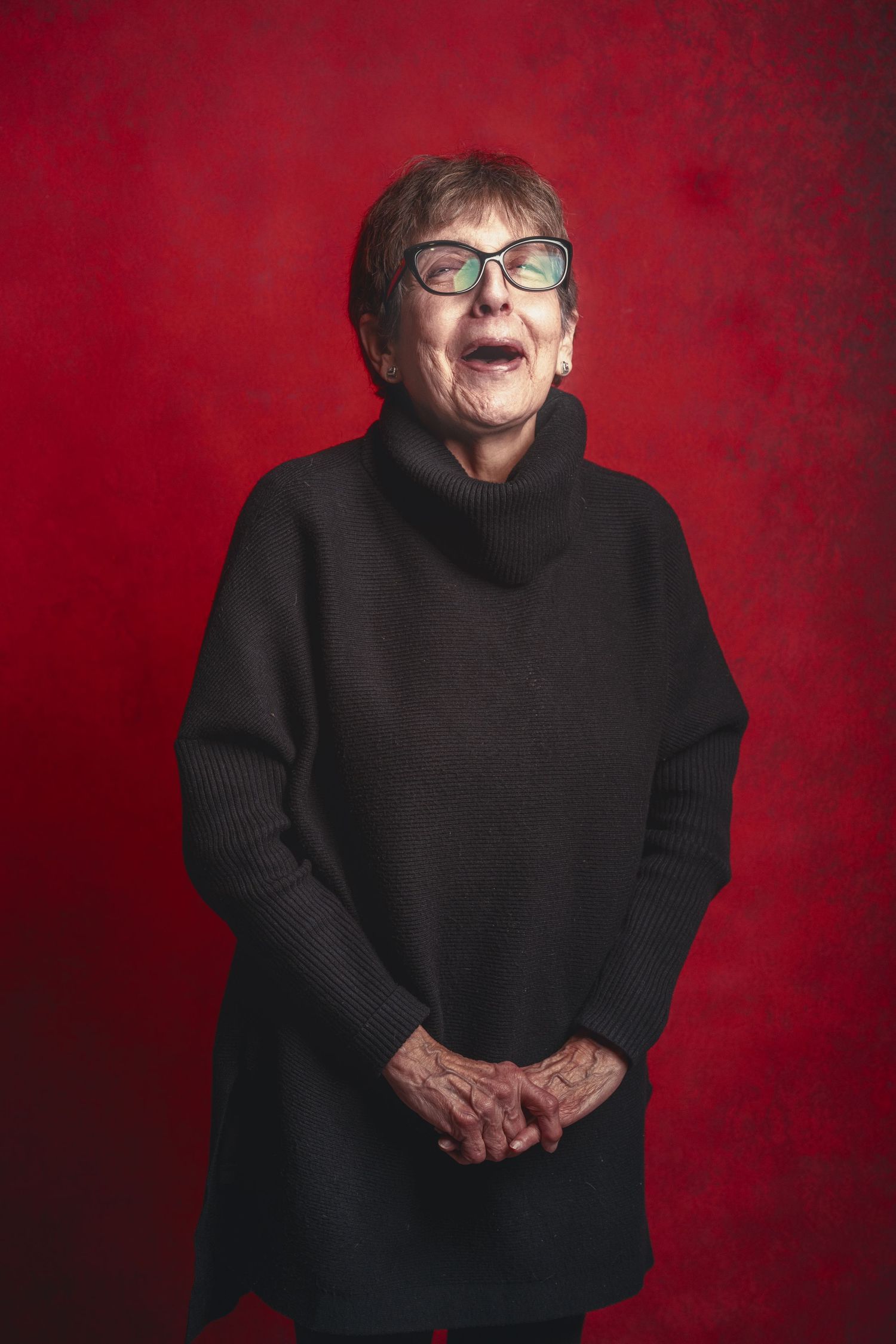 A person wearing a black turtleneck sweater poses against a deep red background in a series of expressive portraits.