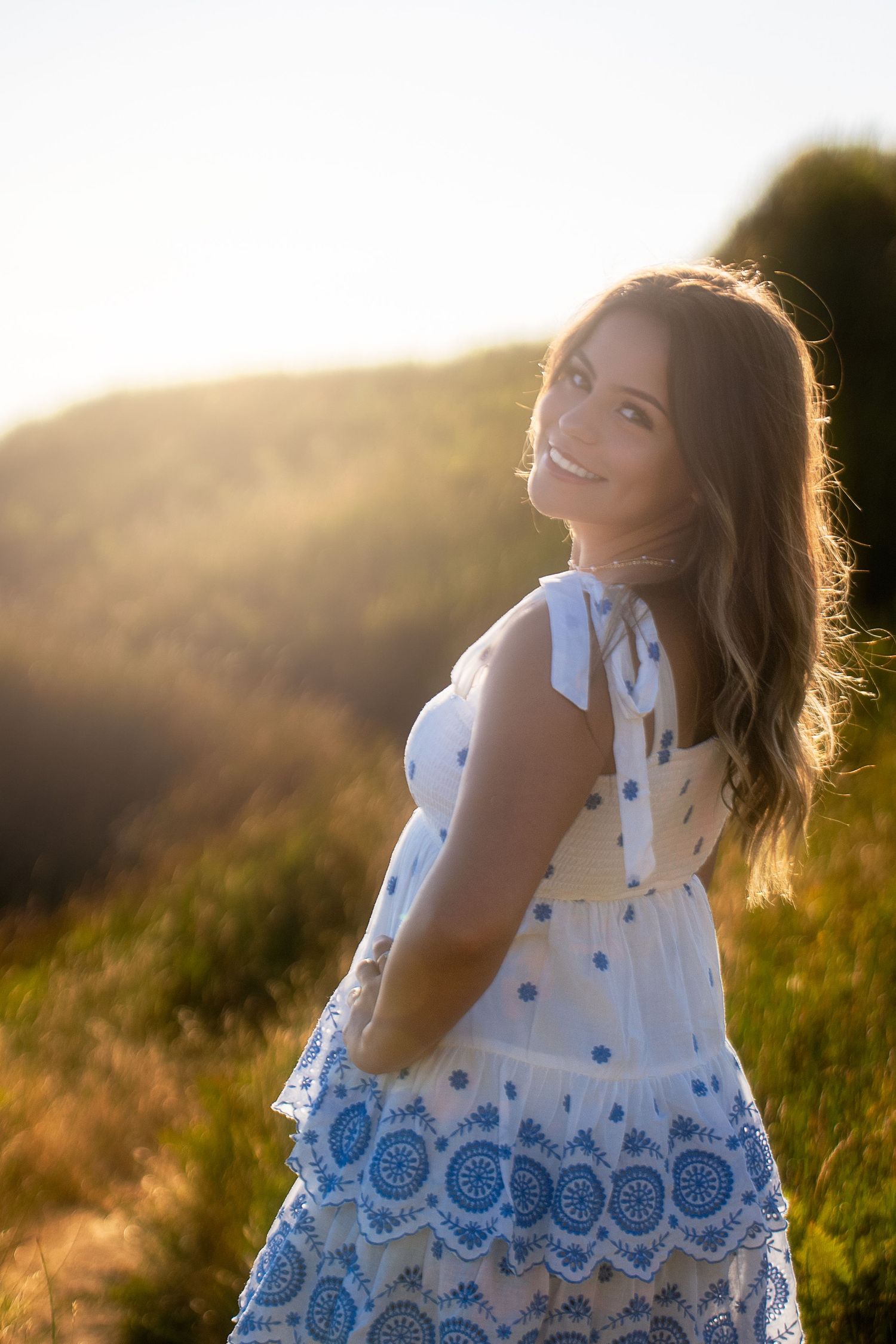 Sunlit portrait of someone in a white and blue embroidered dress during golden hour.