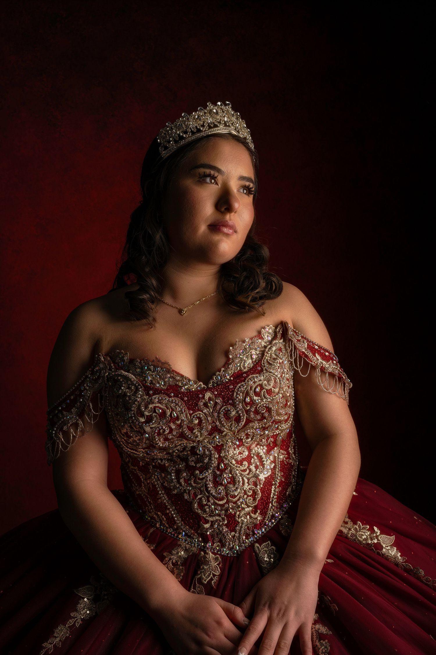 Elegant quinceañera portraits in ornate red gown against dramatic dark background.