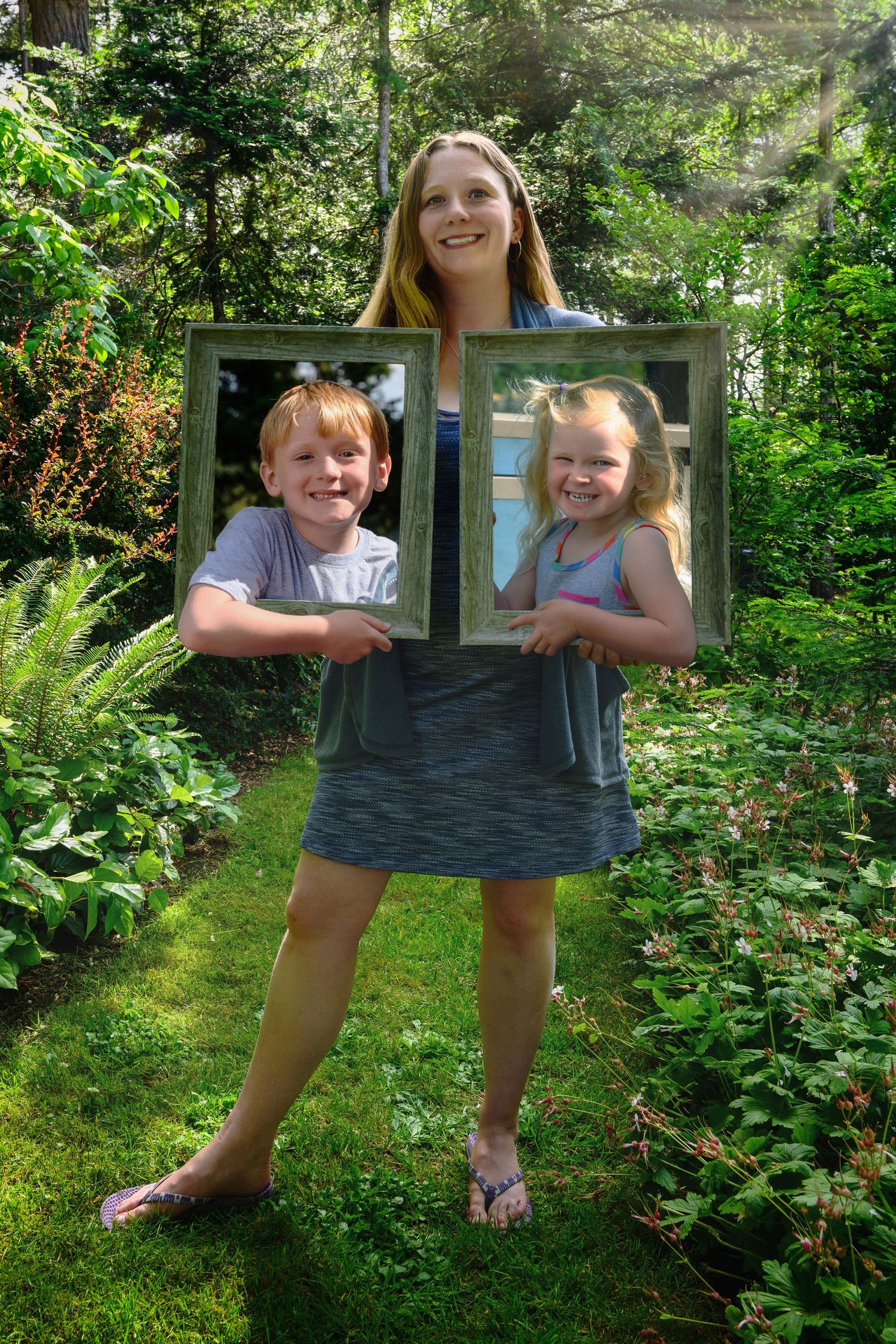 Two people pose playfully with an empty picture frame in a lush garden setting.