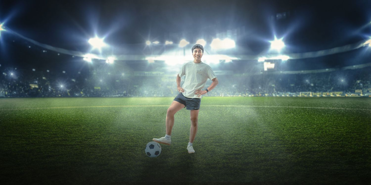 Soccer player poses with ball on illuminated stadium field at night.