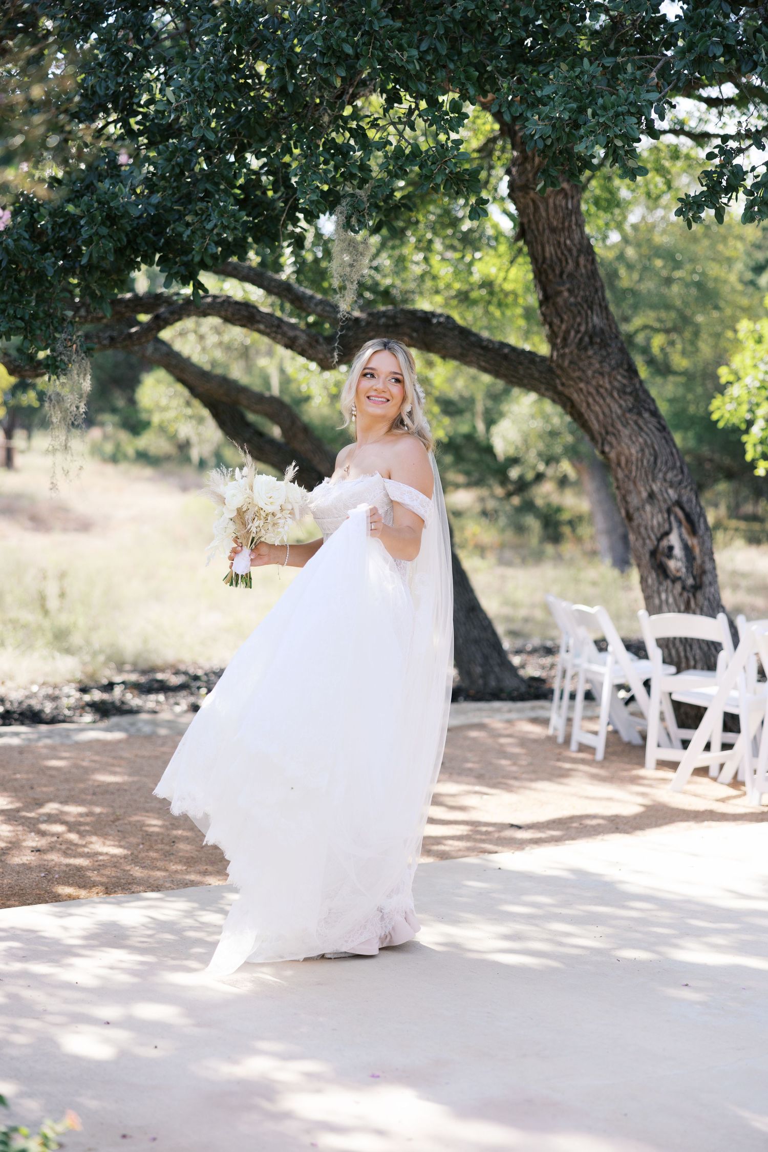 Joyful bride twirls in off-shoulder wedding gown at outdoor garden ceremony site.