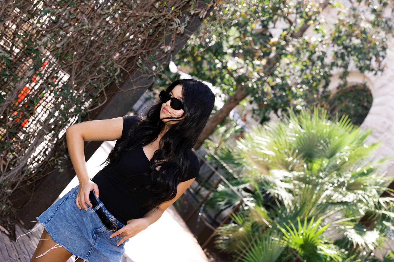 Outdoor fashion shot with palm trees and textured wall backdrop showing casual summer style.