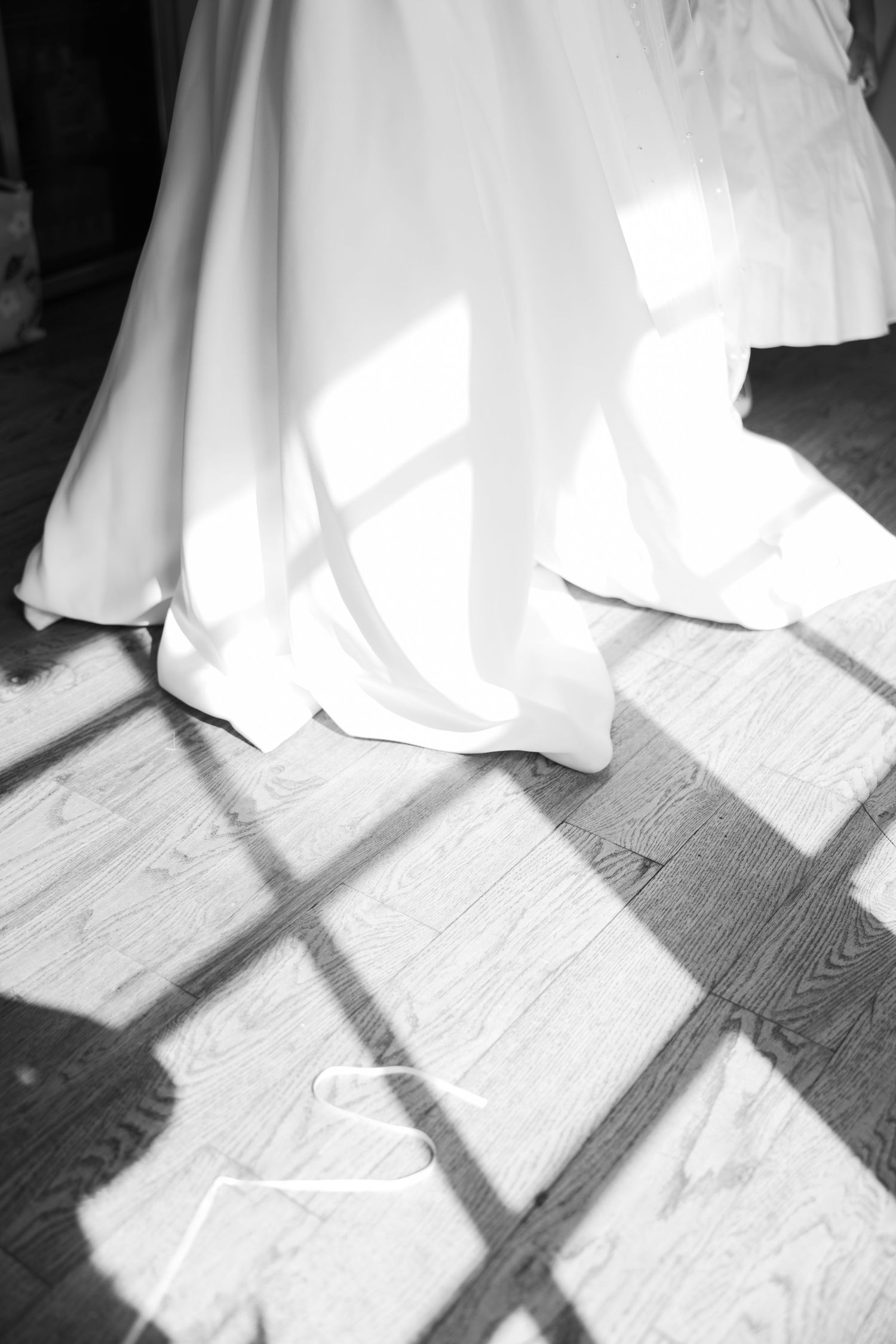 Black and white photo showing shadows cast by a flowing white wedding dress on a wooden floor.