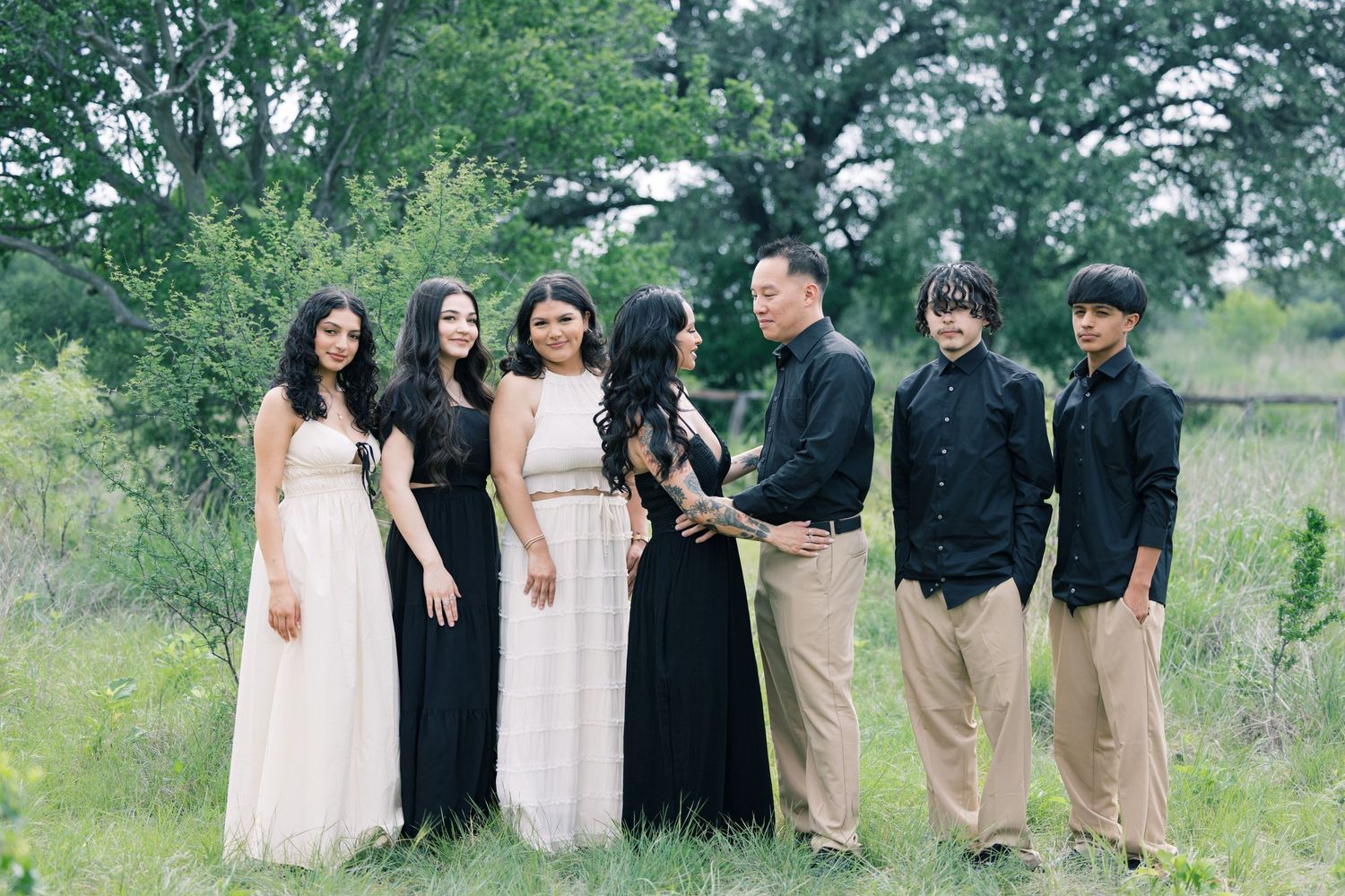 Wedding party poses in natural setting wearing formal black and neutral colored outfits.