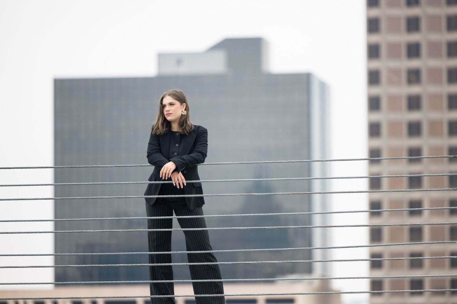 Urban rooftop portrait with metal railings and city buildings in view.