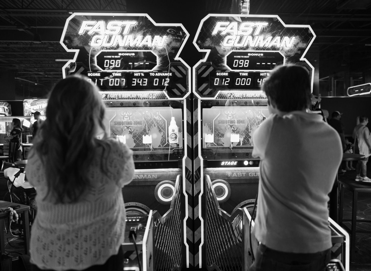 Players at arcade shooting games with Fast and Gunman signage visible.