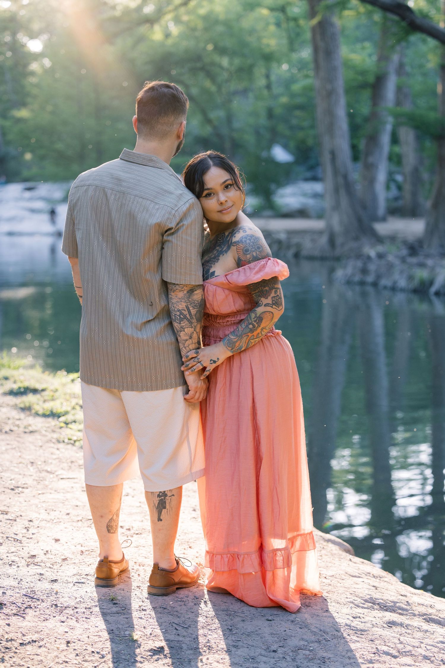 A couple in coordinated outfits stands by a serene lake during golden hour, creating a romantic silhouette.