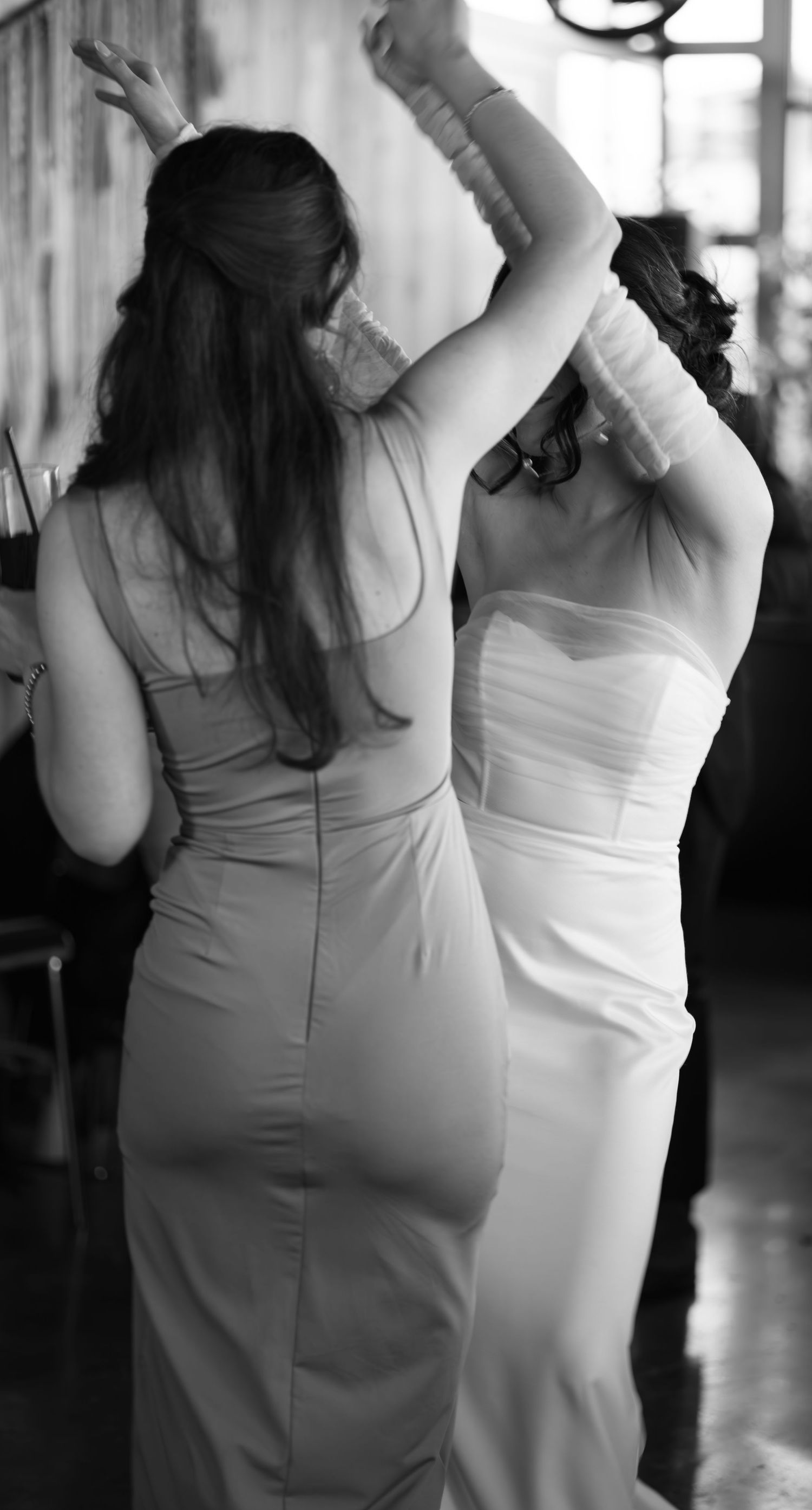 Two women in elegant dresses dancing together at a wedding celebration, captured in black and white.