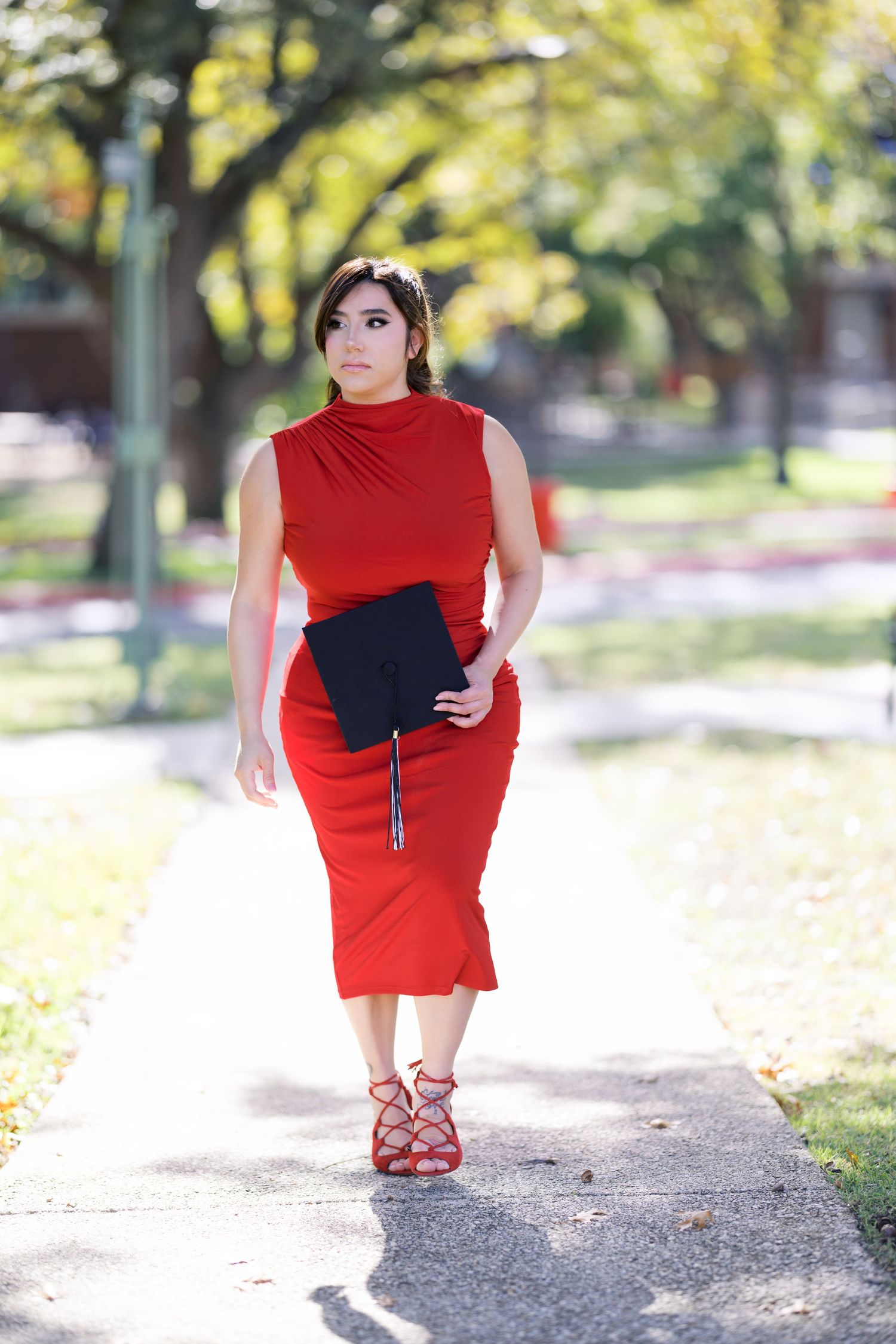 Person in red dress walking on outdoor path holding graduation materials.