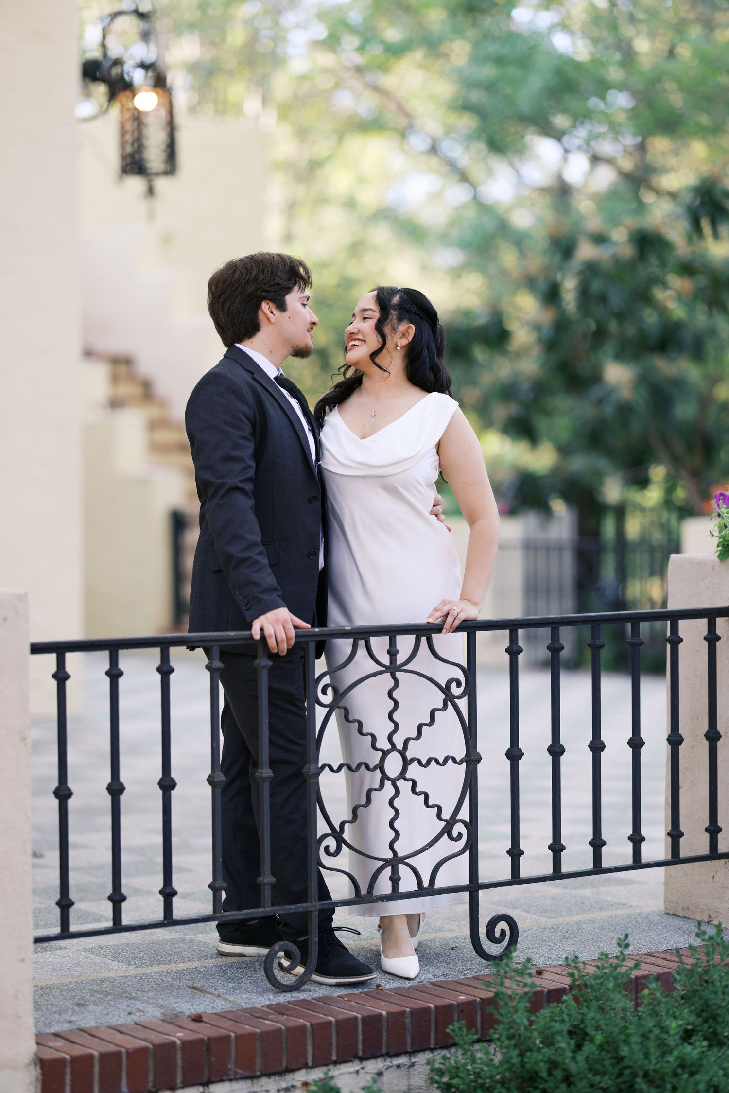Wedding couple poses by decorative iron railings under classical architecture.