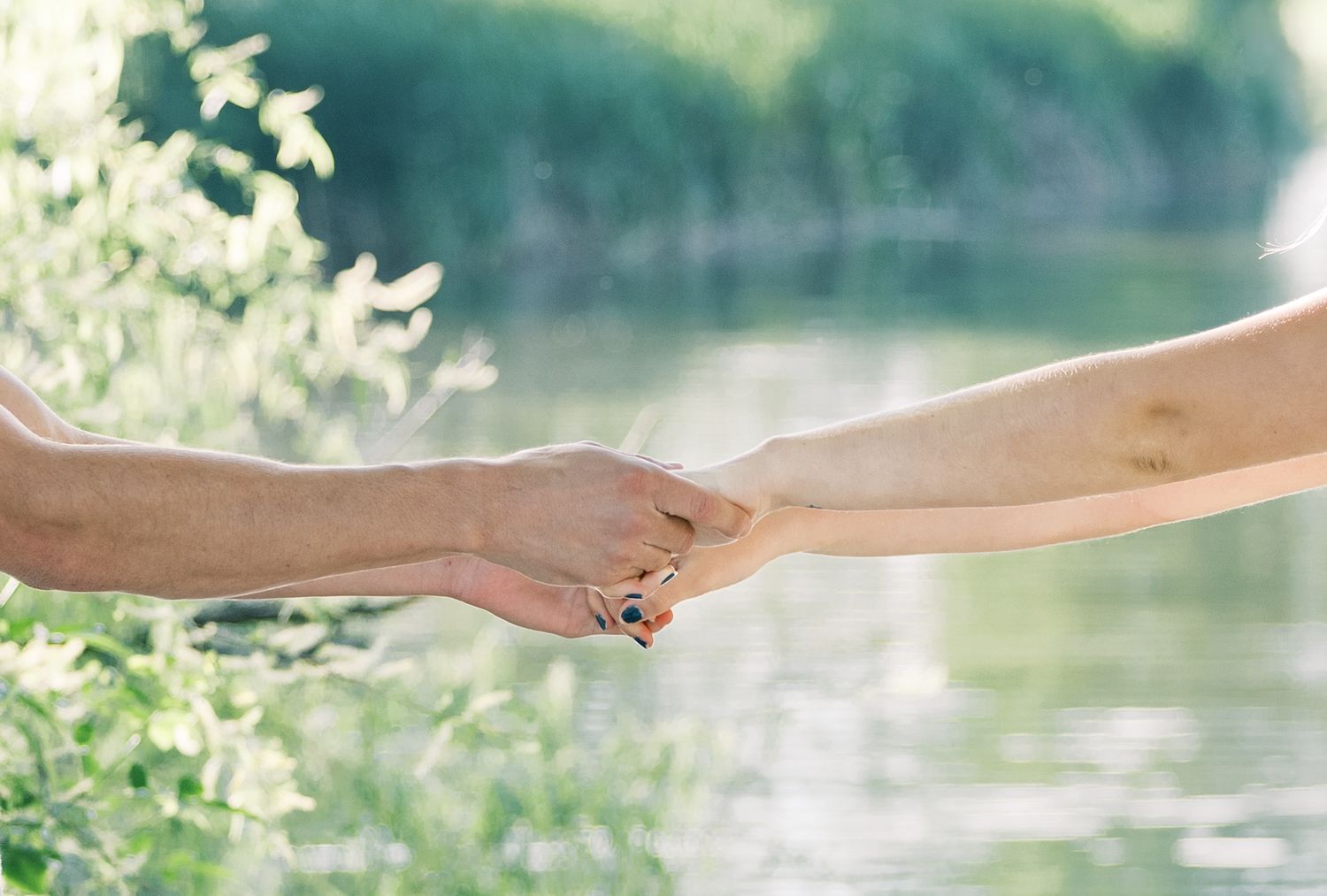 Close-up of two hands gently holding each other against a soft, dreamy waterfront backdrop.