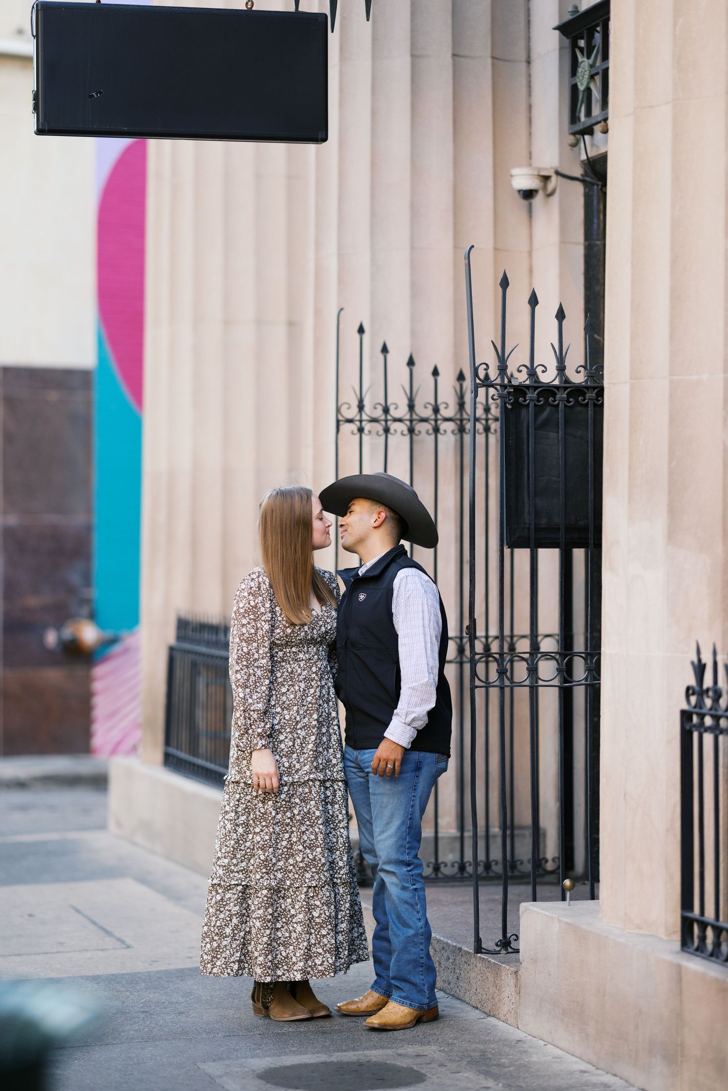 A couple poses playfully in front of a wrought iron gate and stone columns.