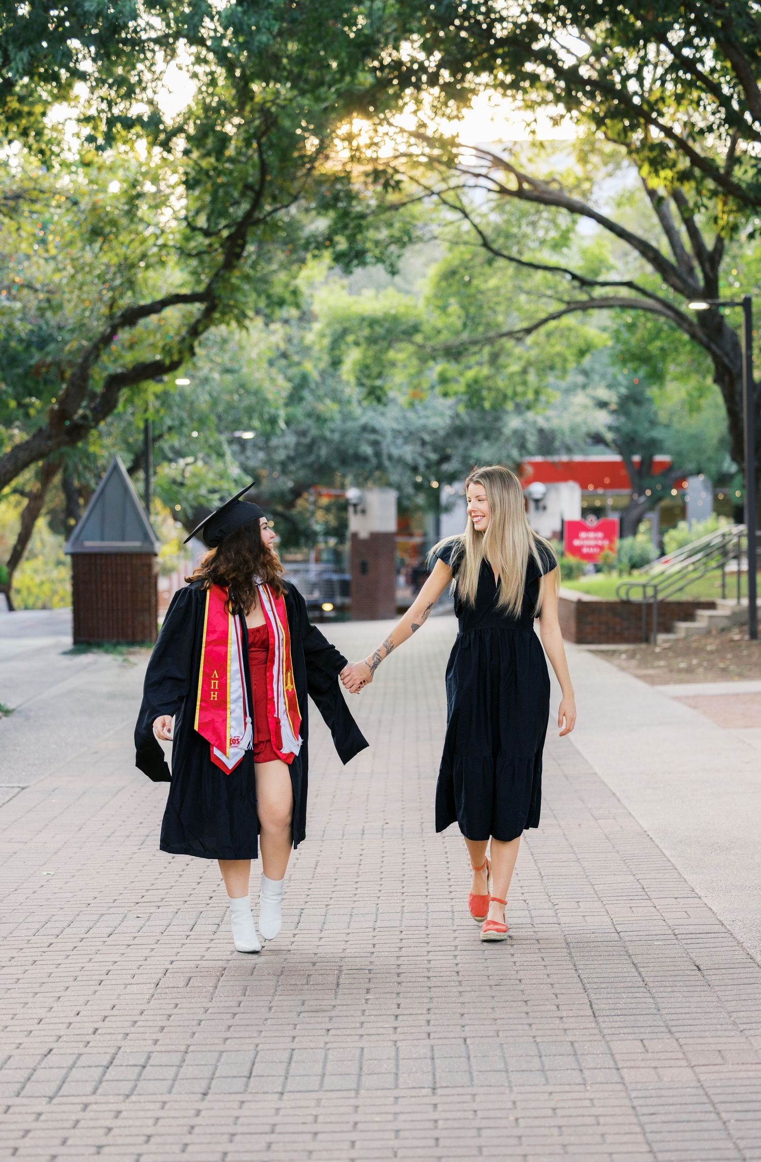 Two friends walking together on campus path during graduation photoshoot.