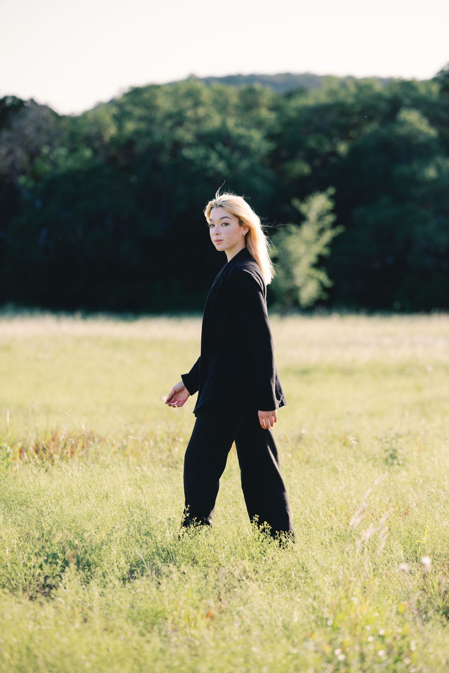 Figure in black ensemble moving dynamically through tall grass in open field.