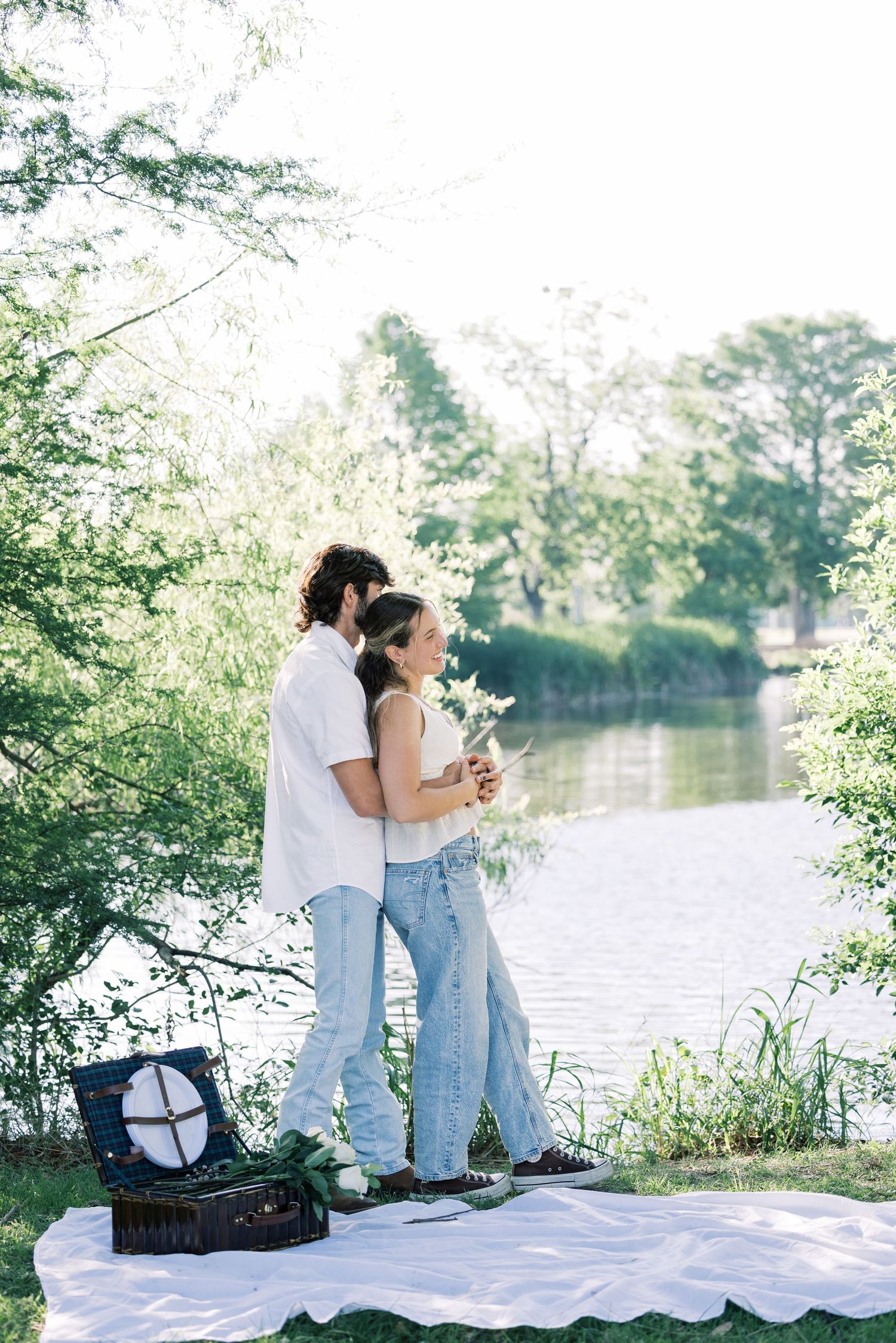 A couple enjoying a romantic moment on a white blanket by the lake with vintage accessories.