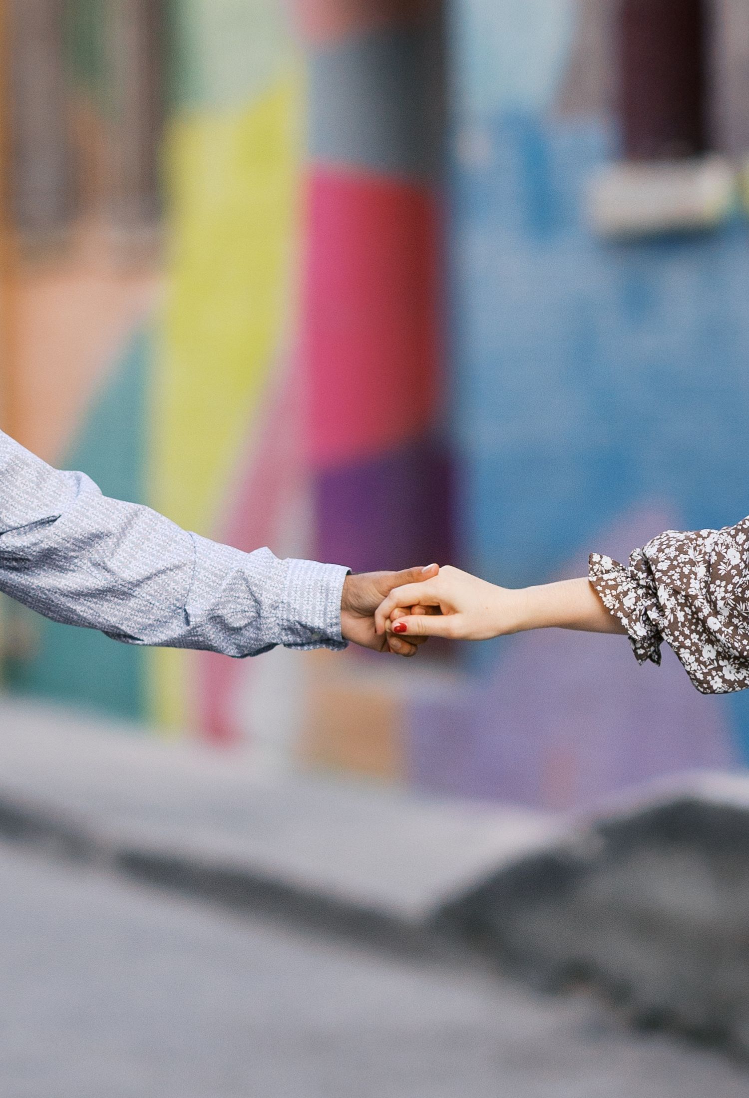 Close-up of hands reaching toward each other against a blurred colorful background.