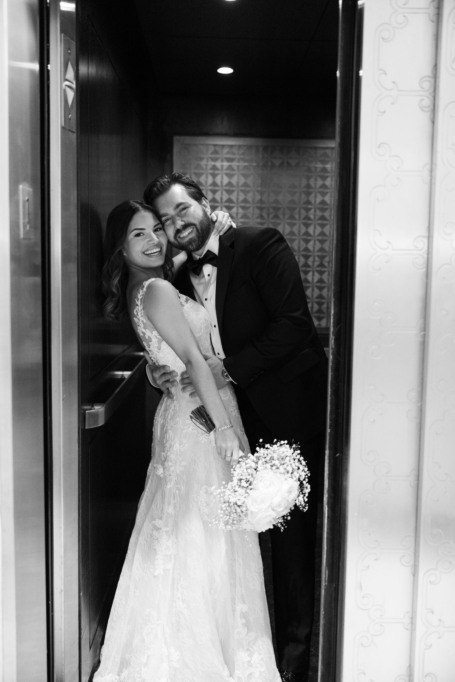 Wedding couple shares joyful moments in black and white near illuminated doorway.