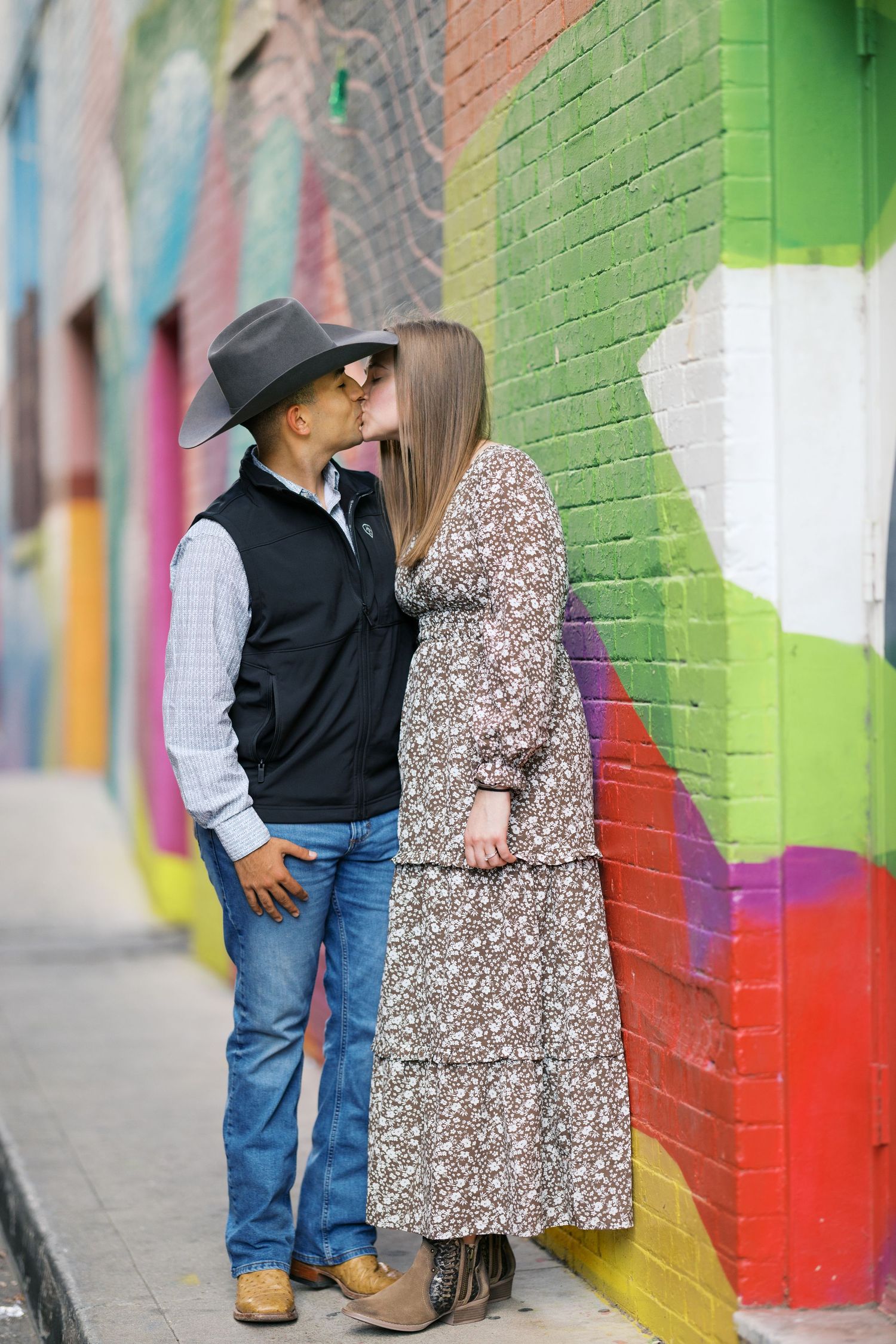 A couple shares an intimate moment against a colorful graffiti wall.