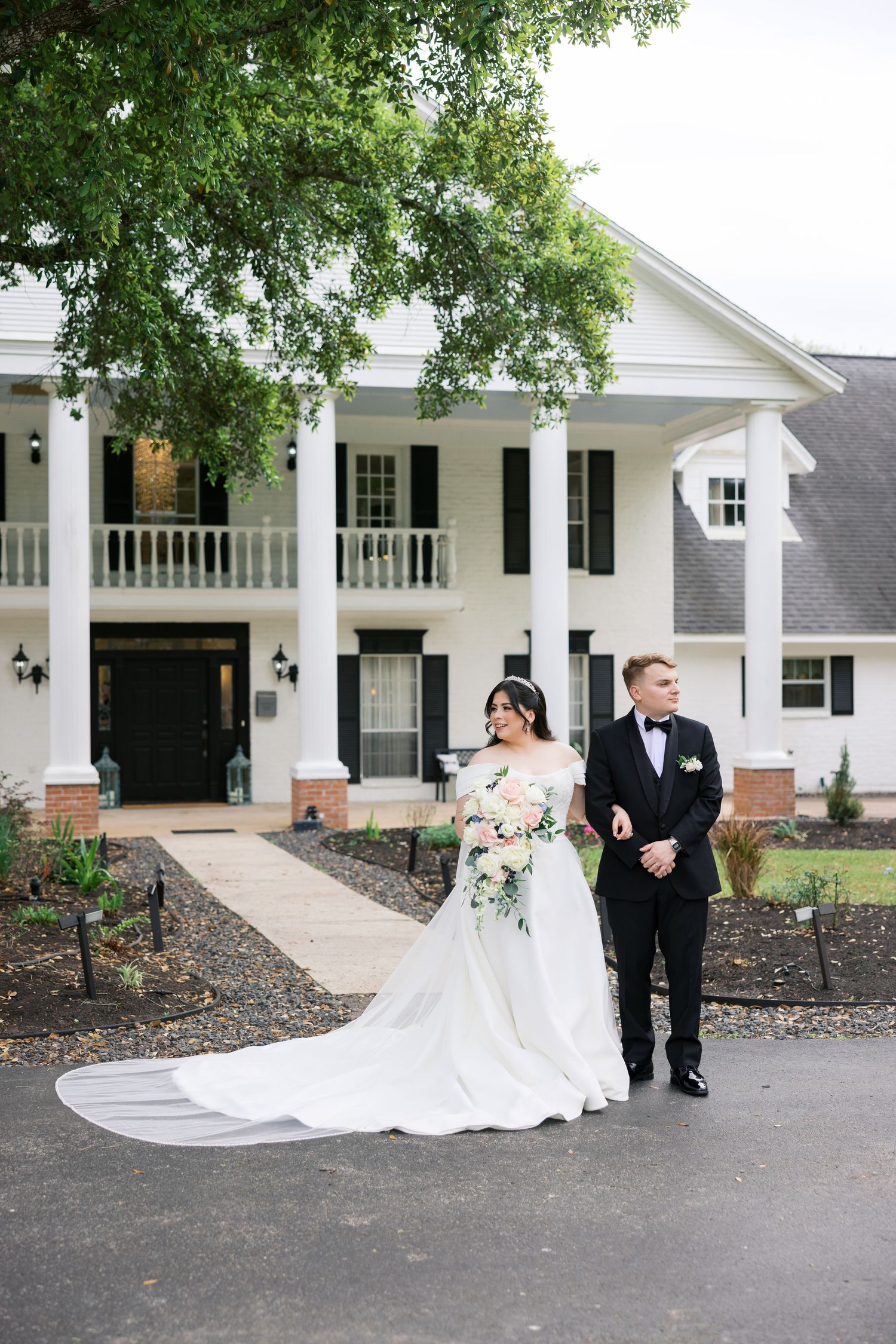 Bride and groom walk hand-in-hand in front of a grand white colonial venue with pillars on their wedding day.