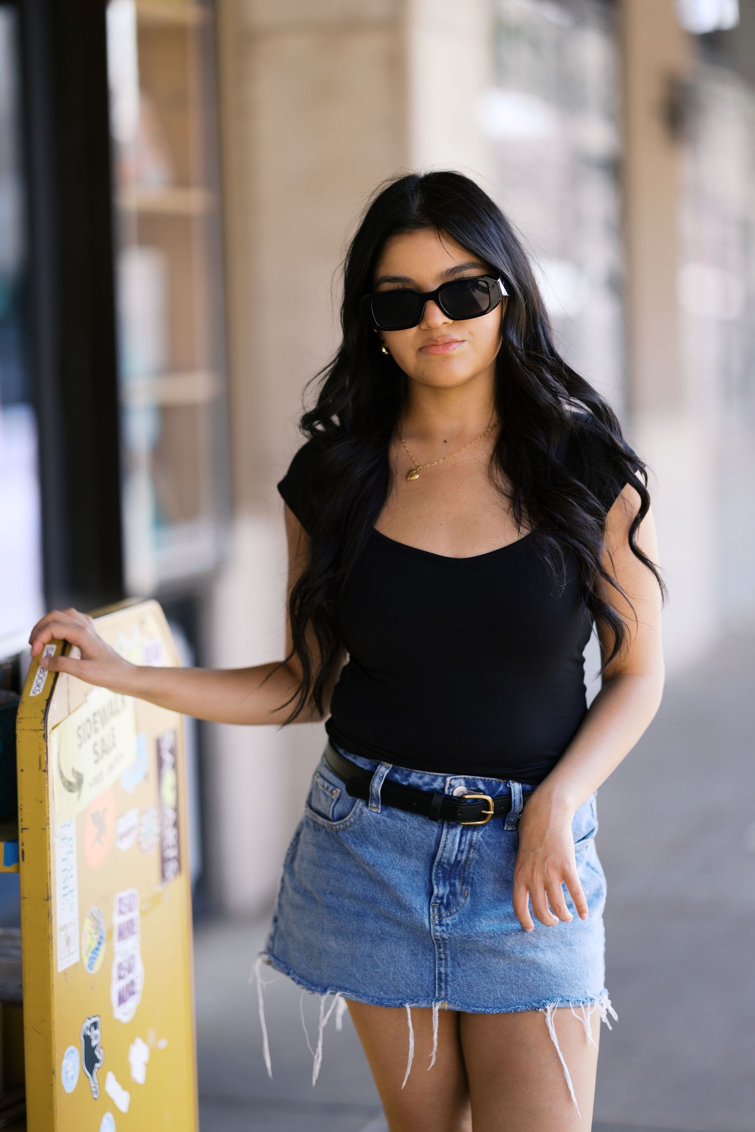 Street style outfit with black tank top and denim skirt posed next to yellow parking meter.