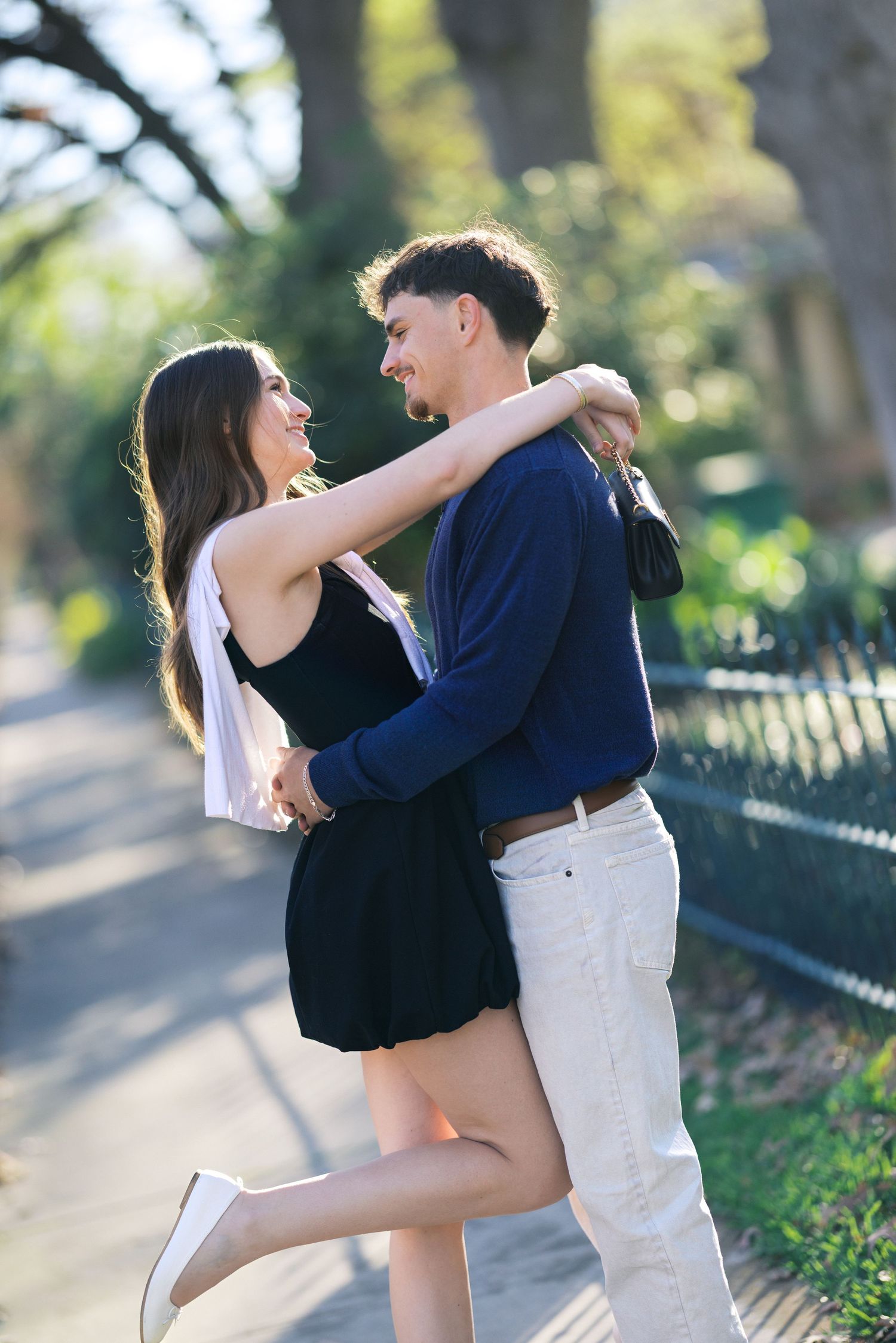 Happy young couple embracing and laughing together on a sunny outdoor pathway in a park.