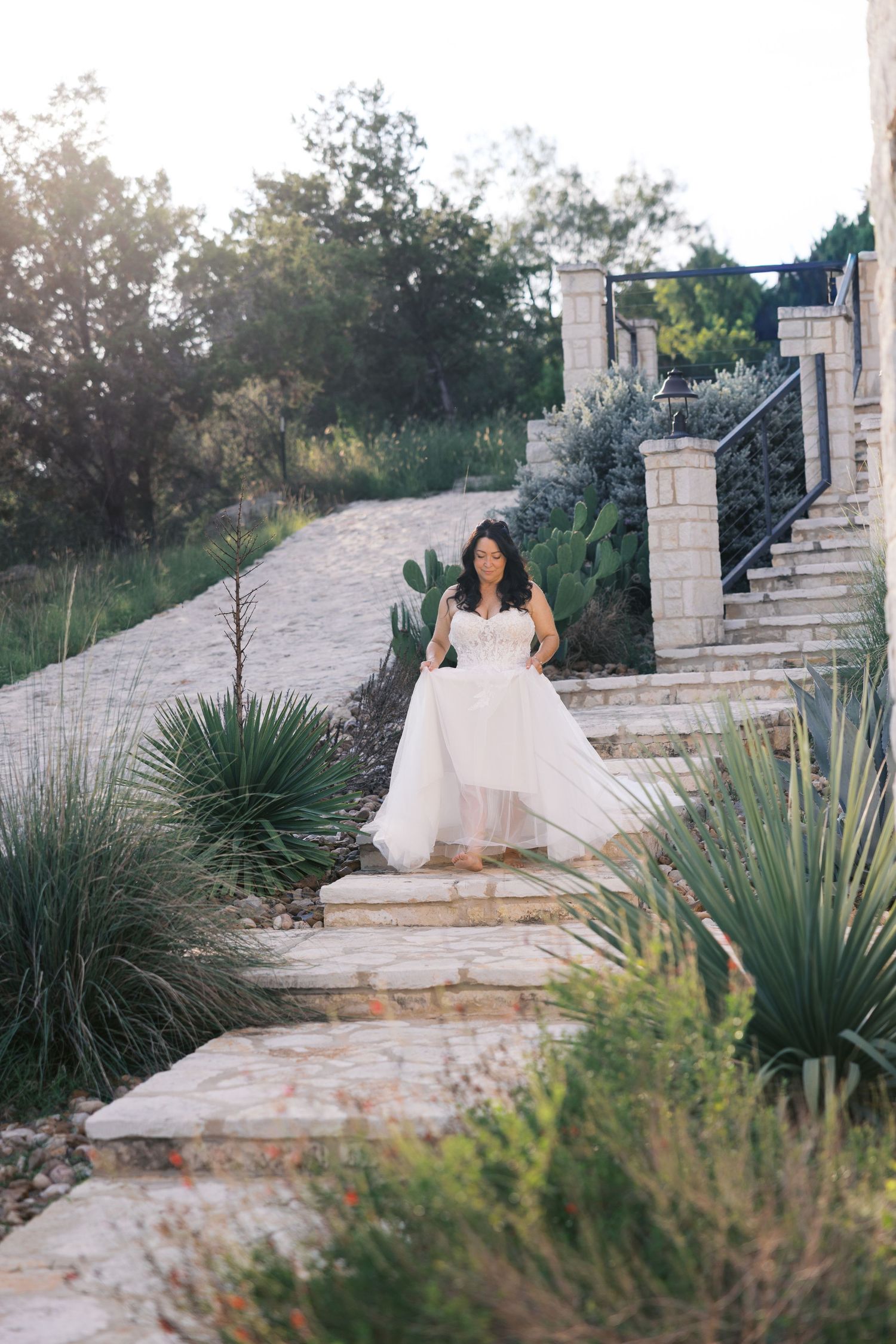 Bride in flowing white dress poses on stone stairway surrounded by desert landscaping.